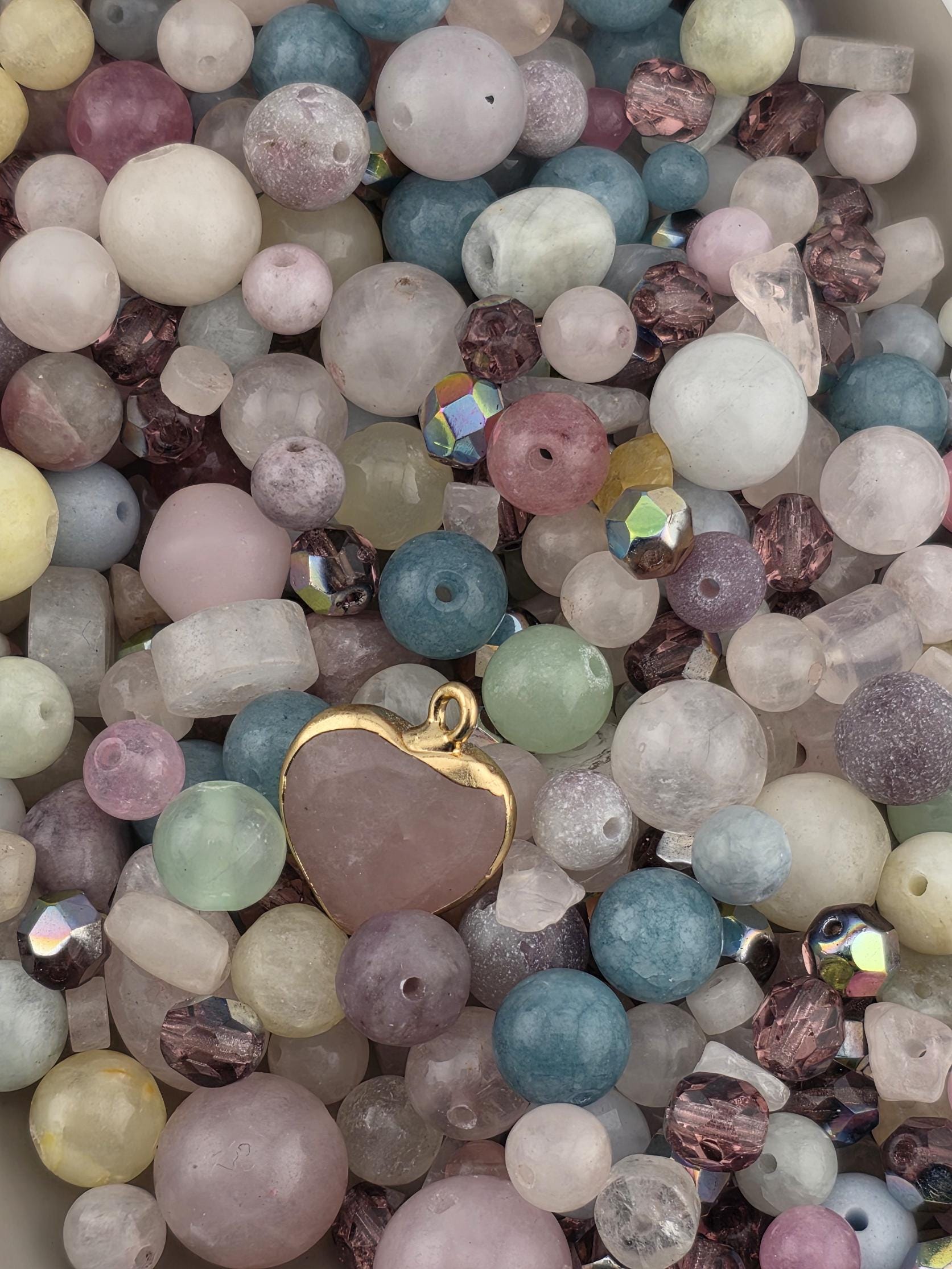 A close-up image of a collection of various colored beads, including clear, pink, blue, green, and purple beads, as well as some with gemstones or crystals.