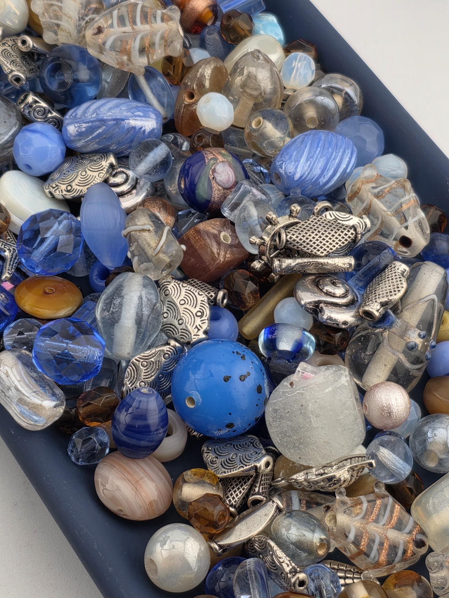The image is a collection of various colorful glass beads and beads, including blue, silver, and clear beads, arranged in a visually appealing manner.