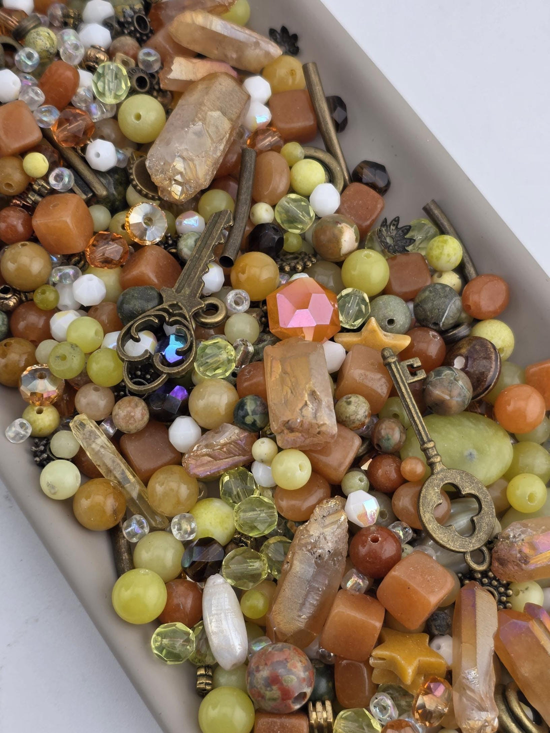 A collection of various beads, gemstones, and metal objects, including a key, arranged in a visually appealing manner.