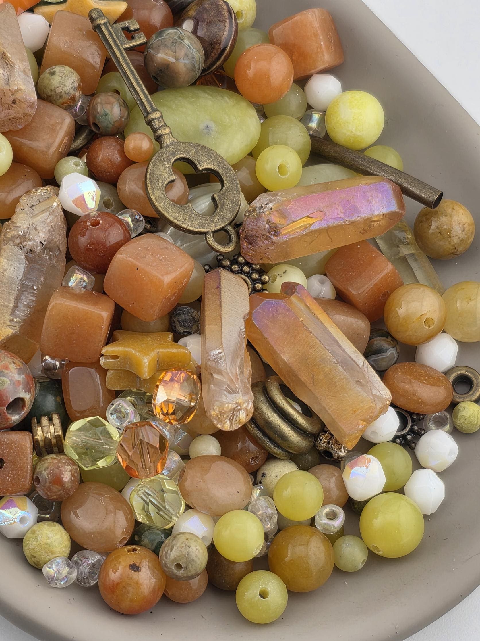 A bowl filled with various beads, gemstones, and other small objects, including a key-shaped object.