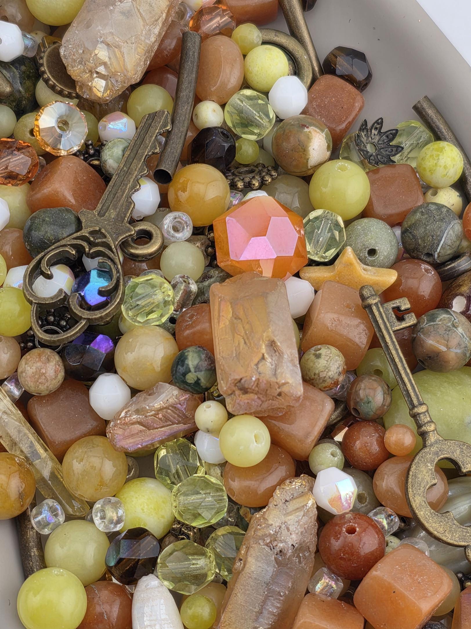 The image is a close-up of a collection of various colorful beads, gemstones, and metal objects, including a key, scattered together.