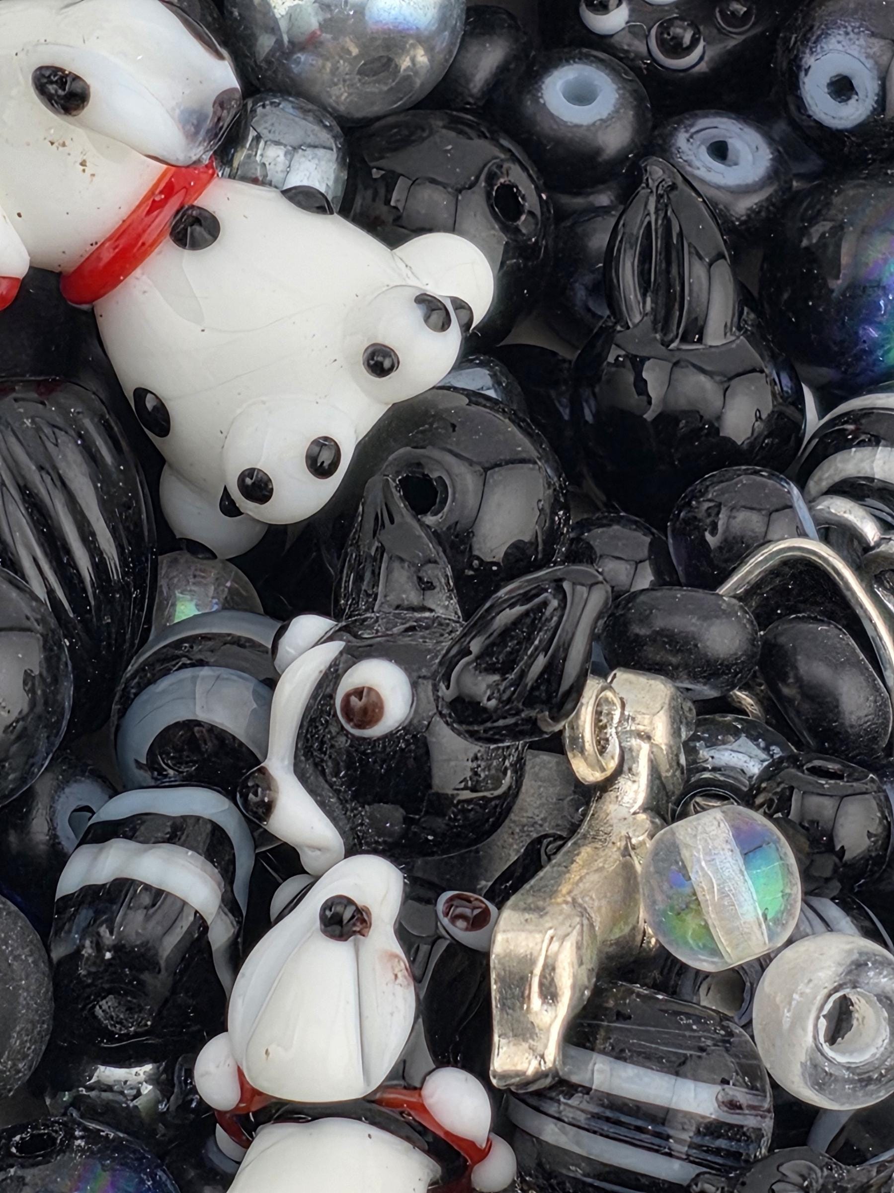 The image is a close-up of a pile of various glass beads, including black and white beads, as well as some with colorful accents.