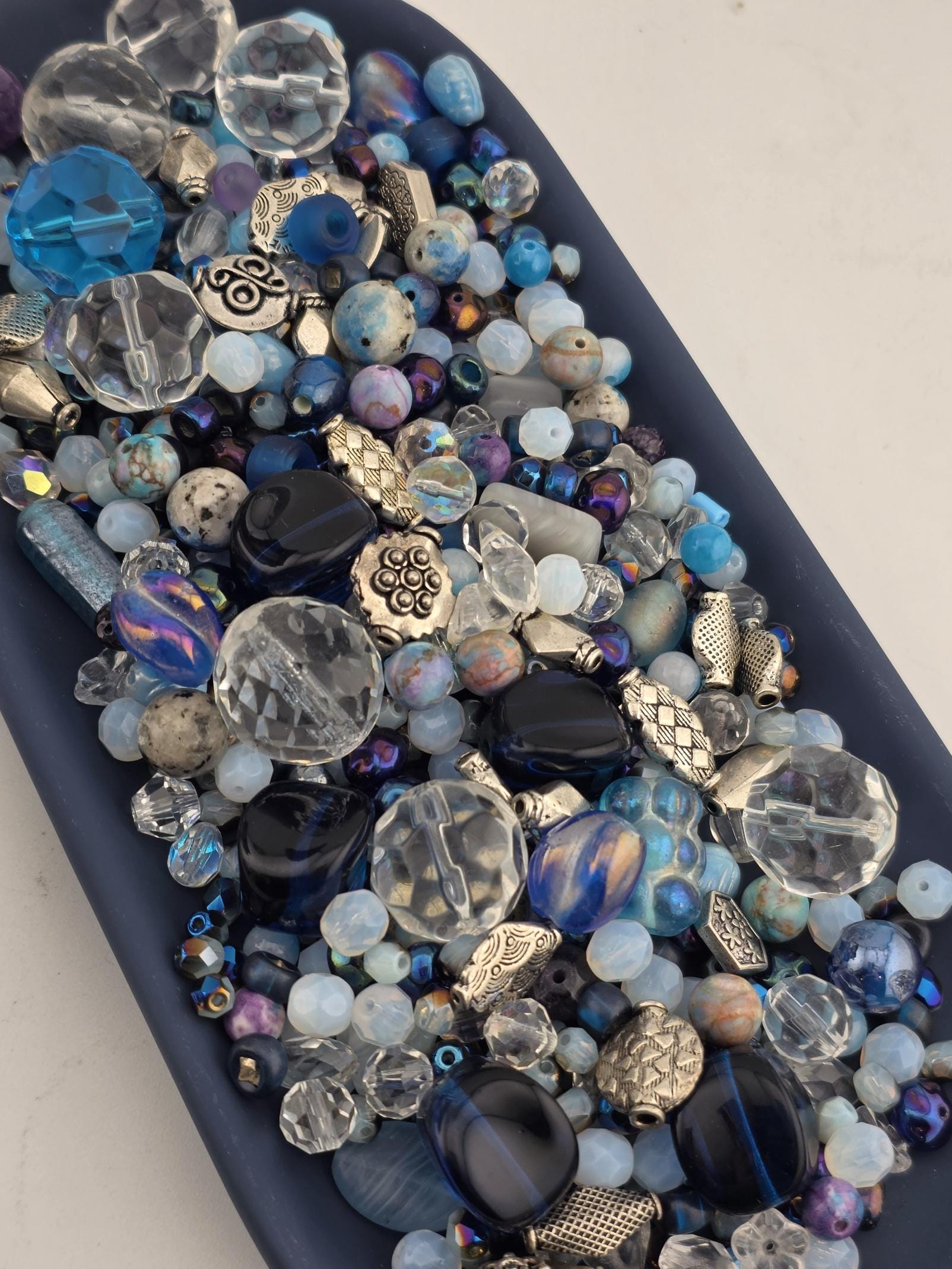 A collection of various colored glass beads and beads in different shapes and sizes, arranged on a dark surface.