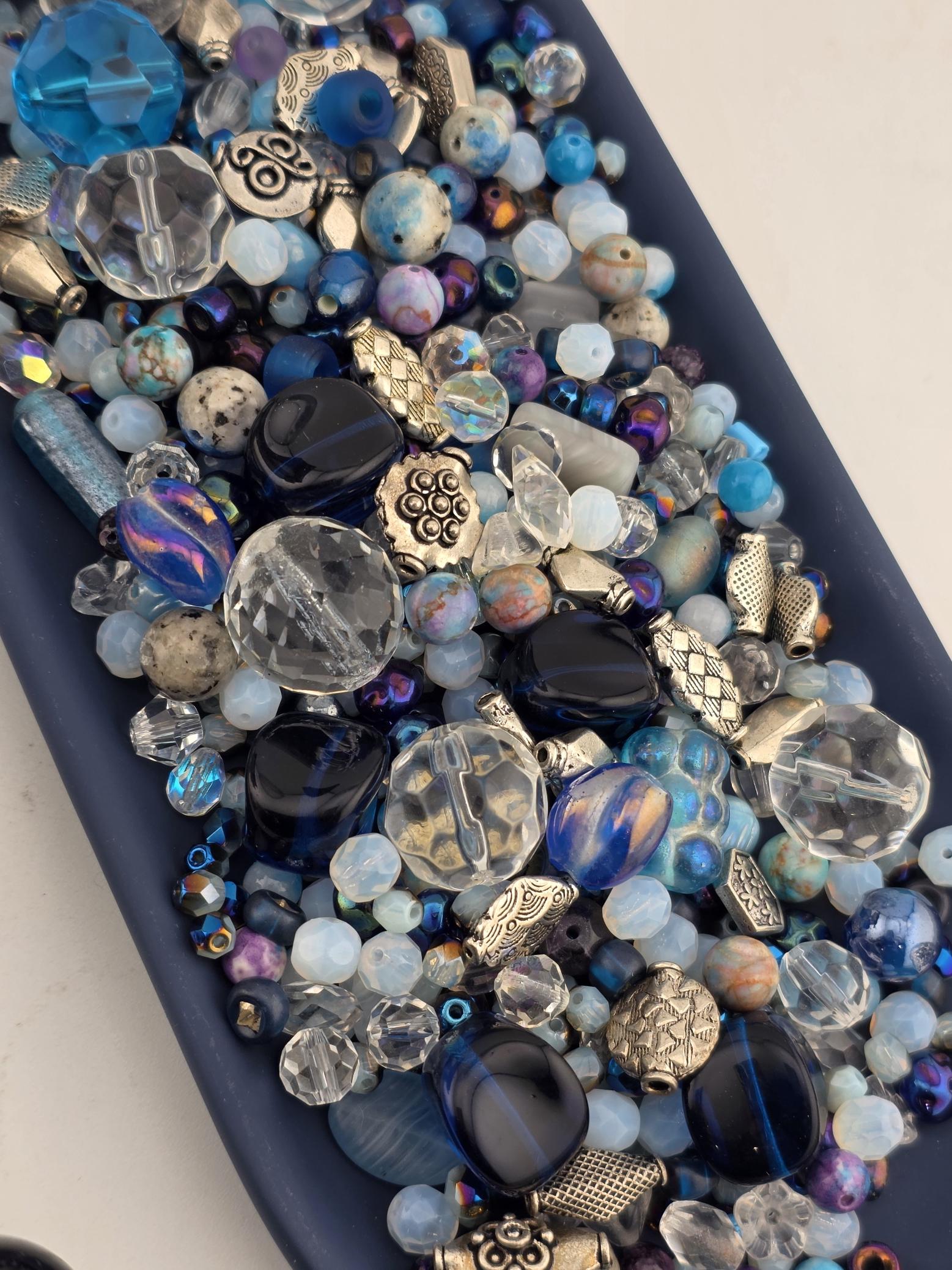 A collection of various colorful beads, including clear, blue, purple, and silver beads, arranged on a surface.