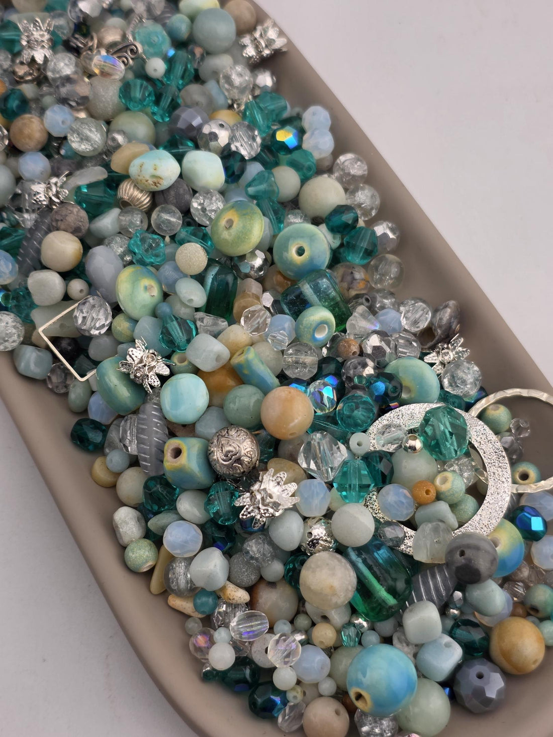 A collection of various colorful beads, including blue, green, and silver, arranged in a tray or container.