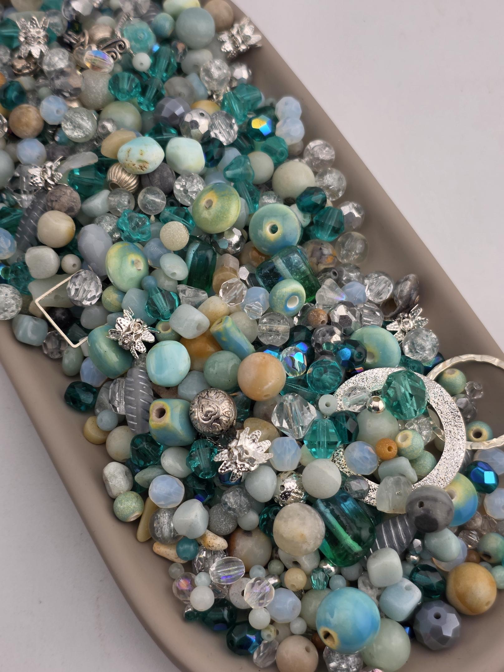 A collection of various colorful beads, including blue, green, and silver, arranged in a tray or container.