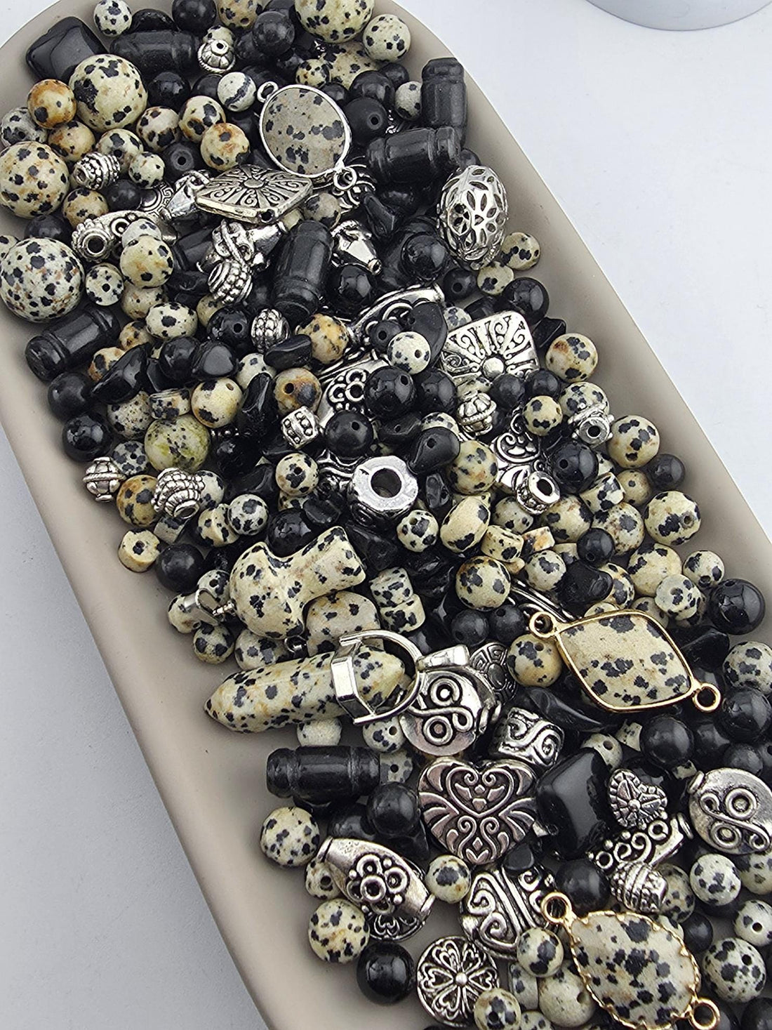 A collection of various beads, charms, and metal pieces in shades of black, white, and gold, arranged on a surface.