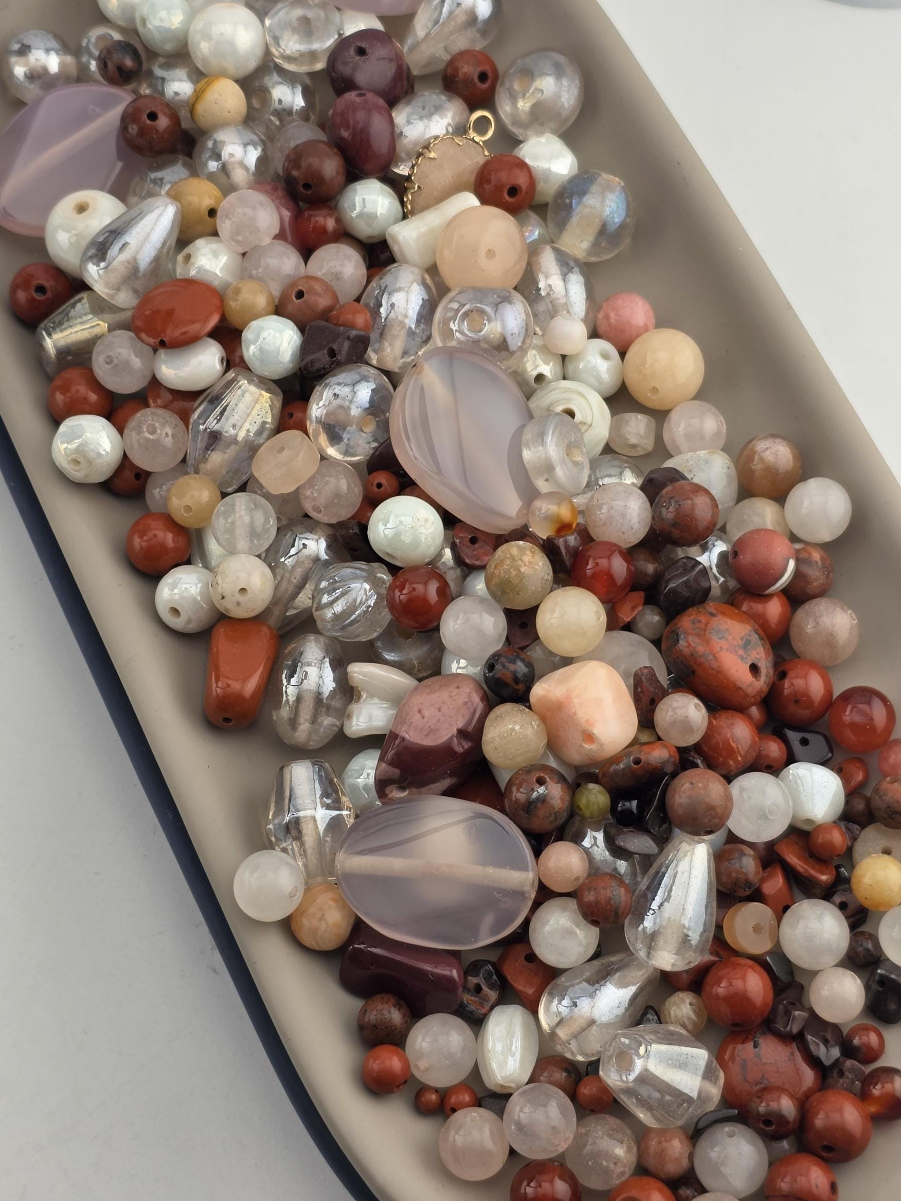 A collection of various beads, including clear, white, and multicolored glass beads, as well as some larger beads made of different materials, such as wood and metal. The beads are scattered across a surface, creating a visually appealing and diverse assortment of colors and textures.