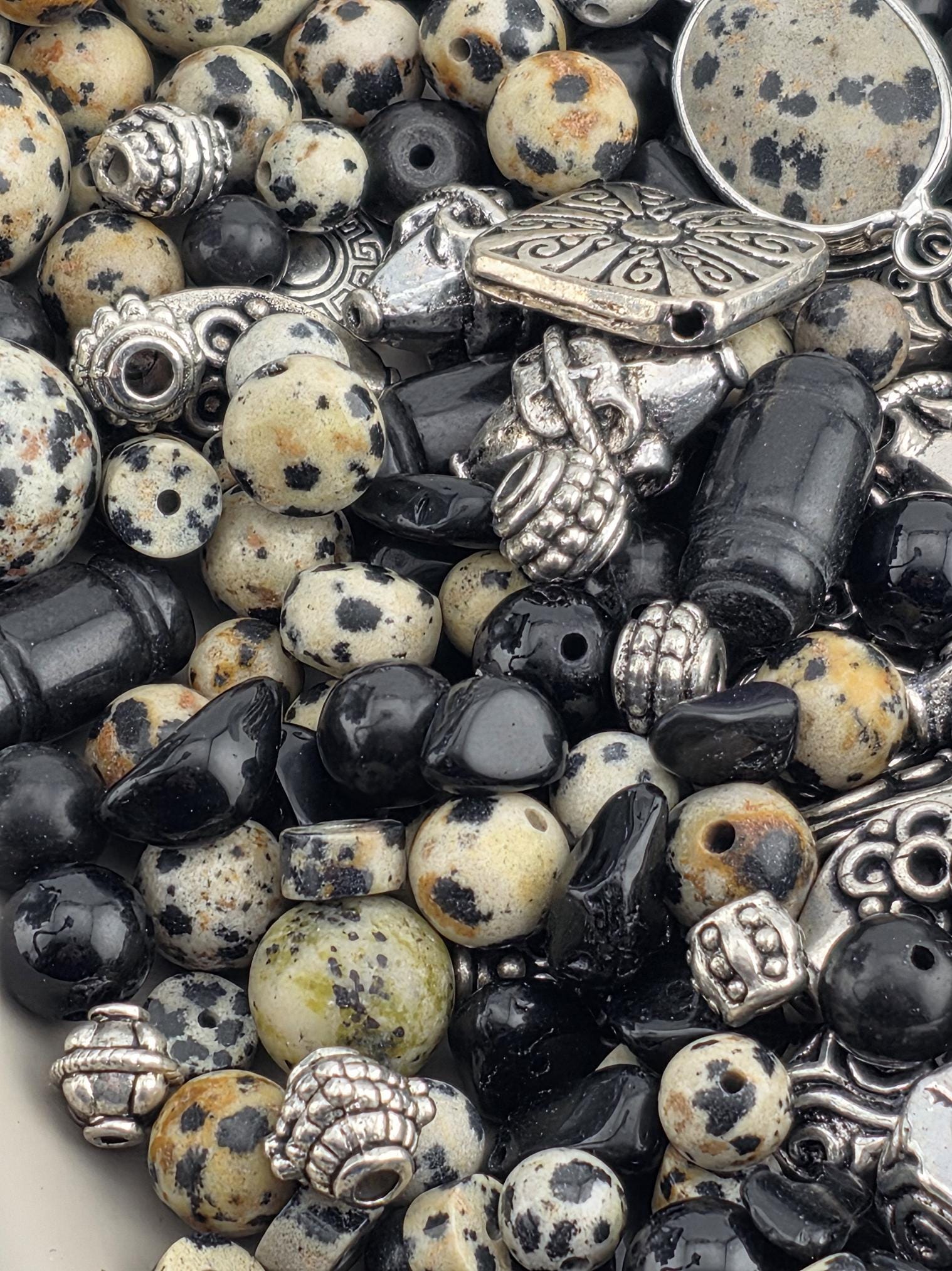 The image is a close-up of various beads and charms, including black and white beads, silver and black beads, and other decorative elements.