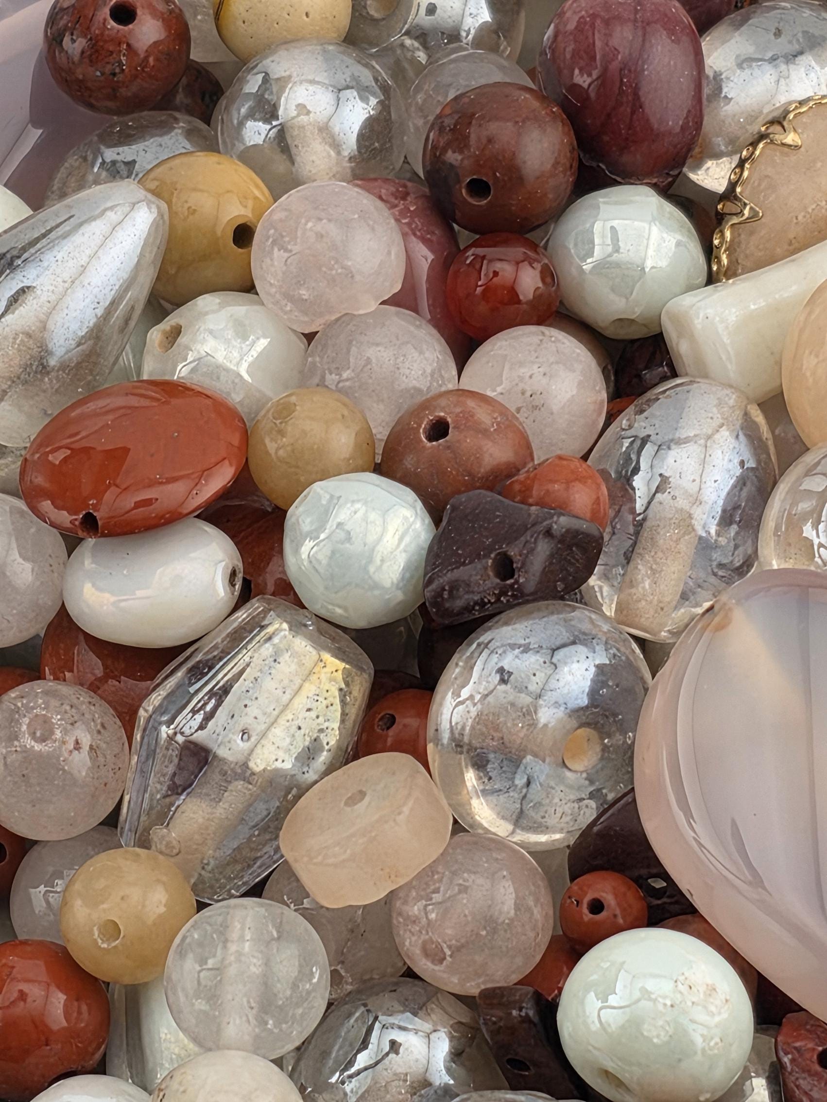 The image is a close-up of various glass beads and stones, including clear, white, brown, and multicolored beads, as well as some larger stones.