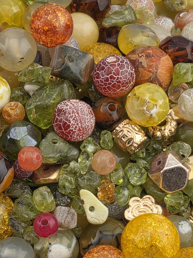 The image is a close-up of a variety of colorful glass beads and stones, including multicolored glass beads, multicolored stones, and some with intricate patterns.