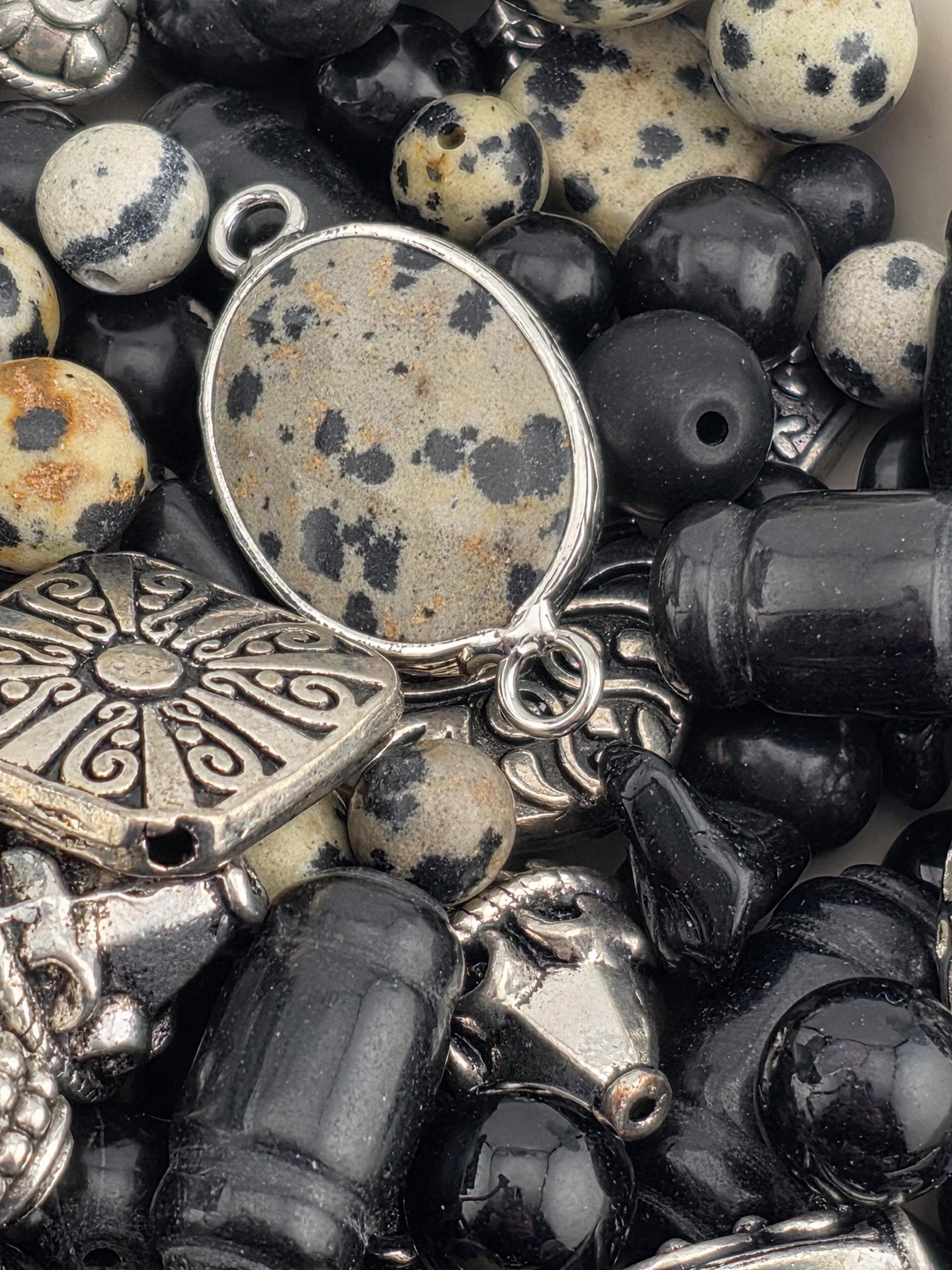 The image is a close-up of various beads, charms, and metal pieces, including black and white beads, silver and black charms, and black and silver beads.