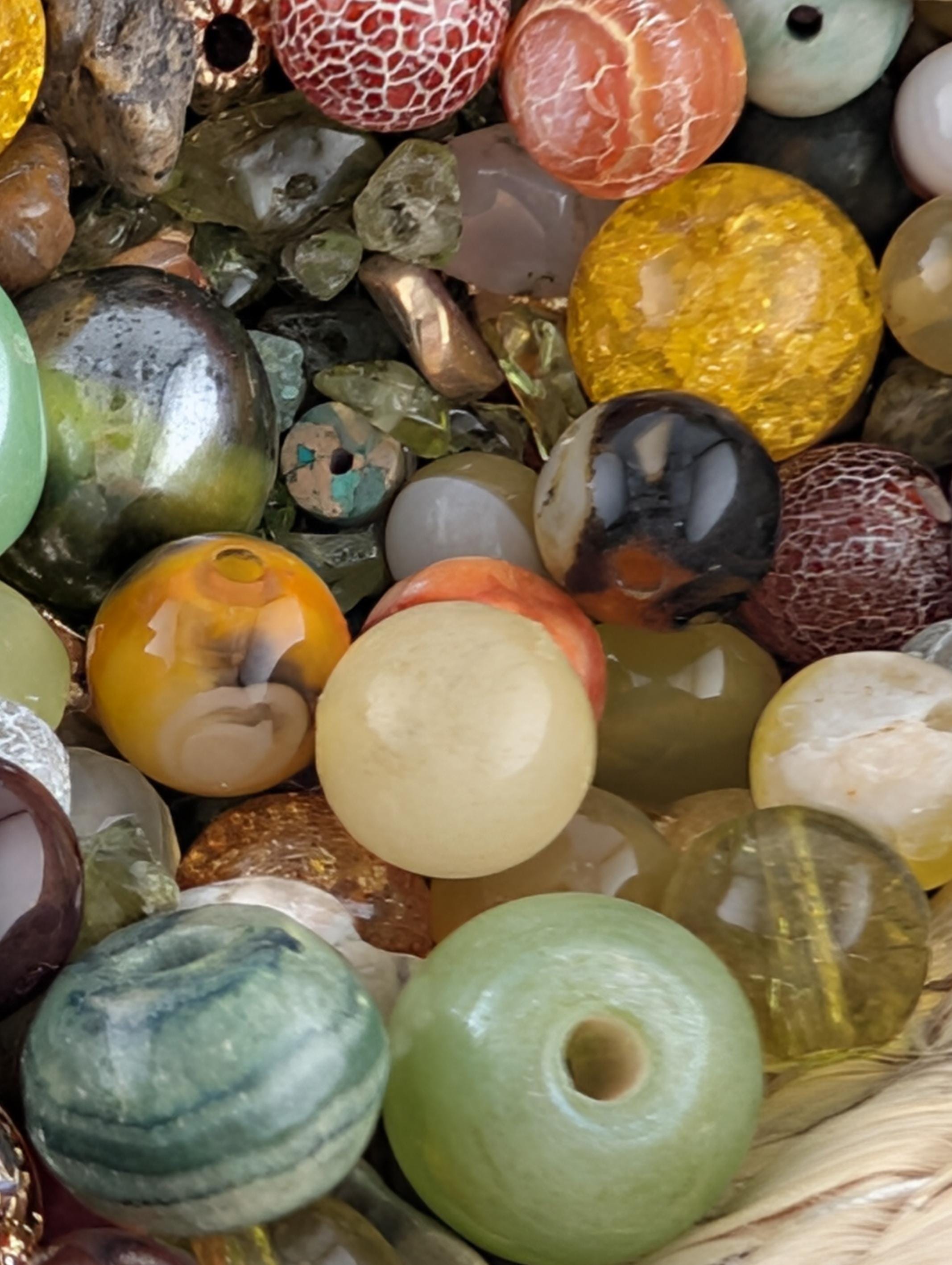The image is a close-up of a collection of various colorful beads, stones, and glass objects, including glass beads, stones, and glass balls, arranged in a visually appealing manner.