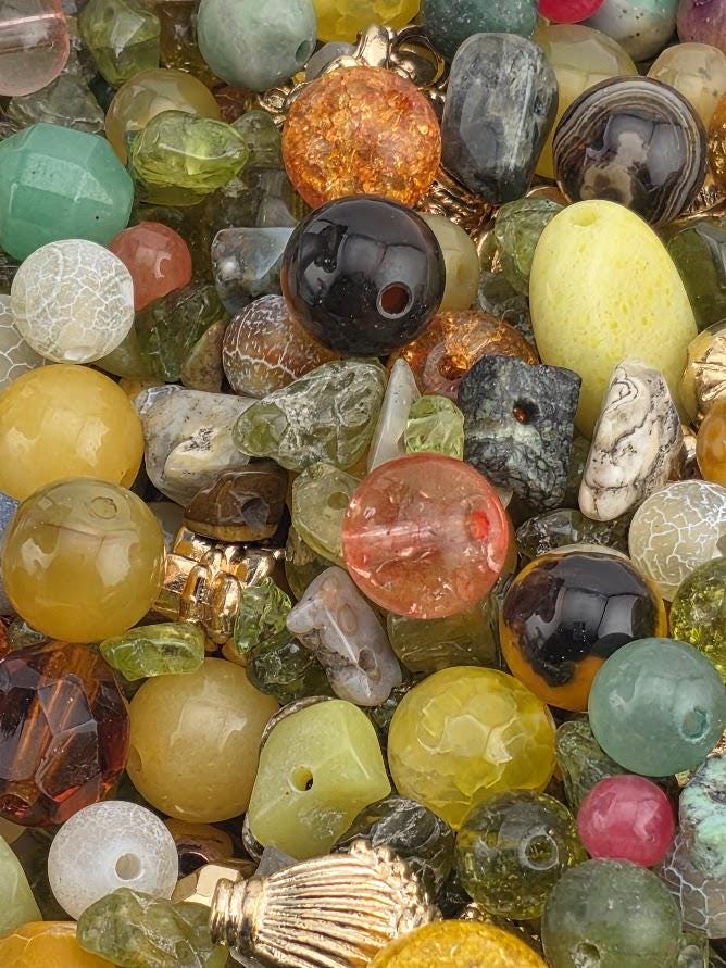 The image is a close-up of a variety of colorful beads and gemstones, including glass beads, gemstones, and other decorative elements.