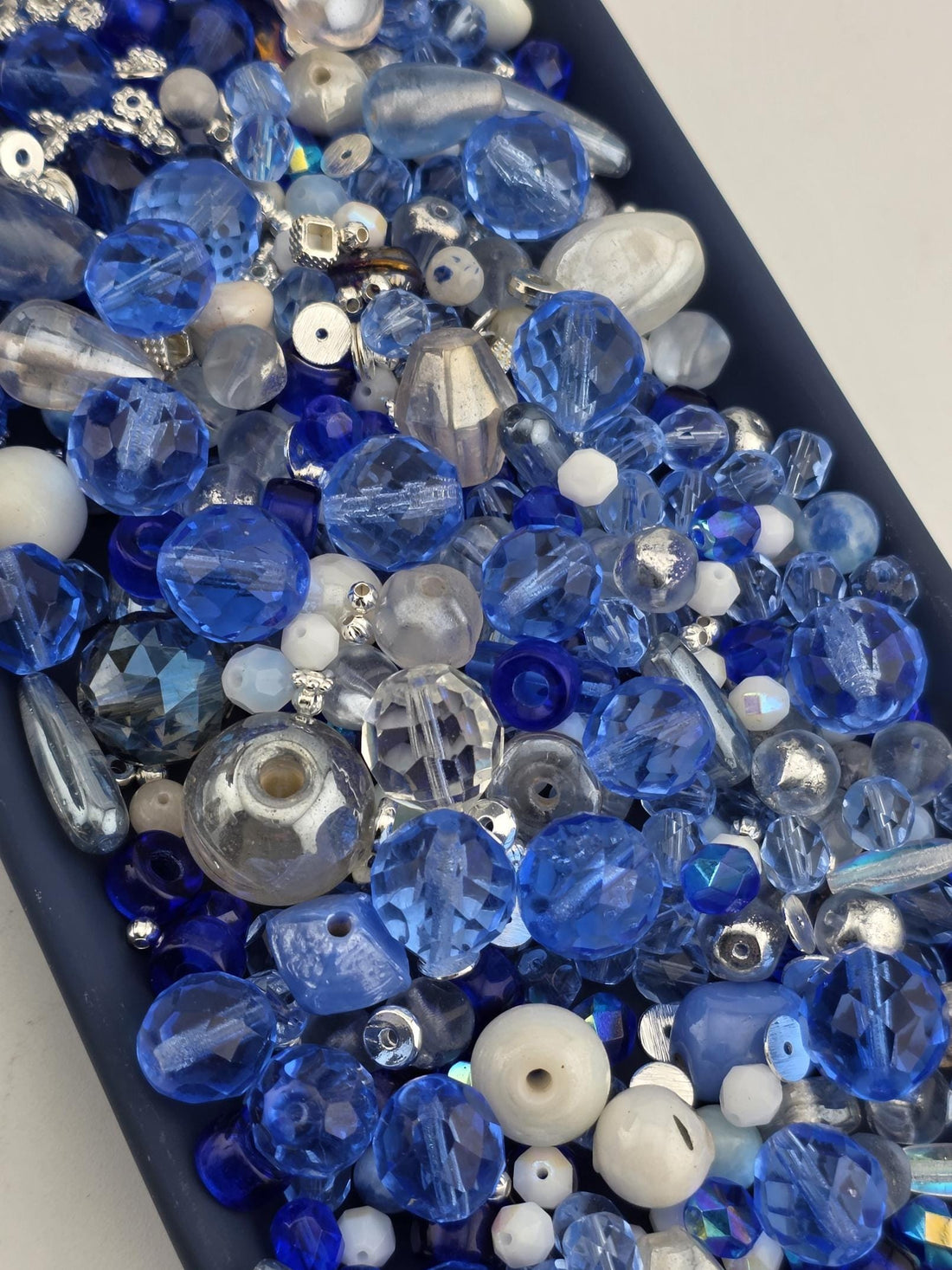 A collection of various blue and silver glass beads, including clear, blue, and silver beads, arranged in a visually appealing manner.