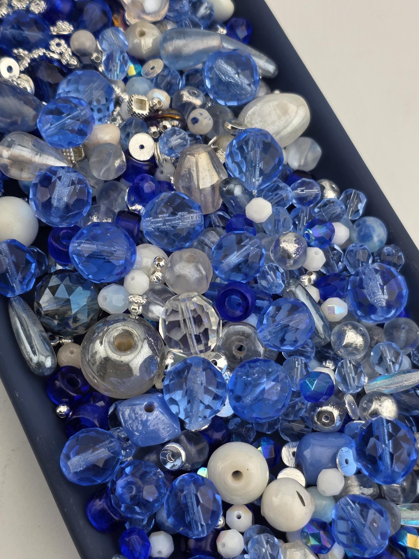 A collection of various blue and silver glass beads, including clear, blue, and silver beads, arranged in a visually appealing manner.