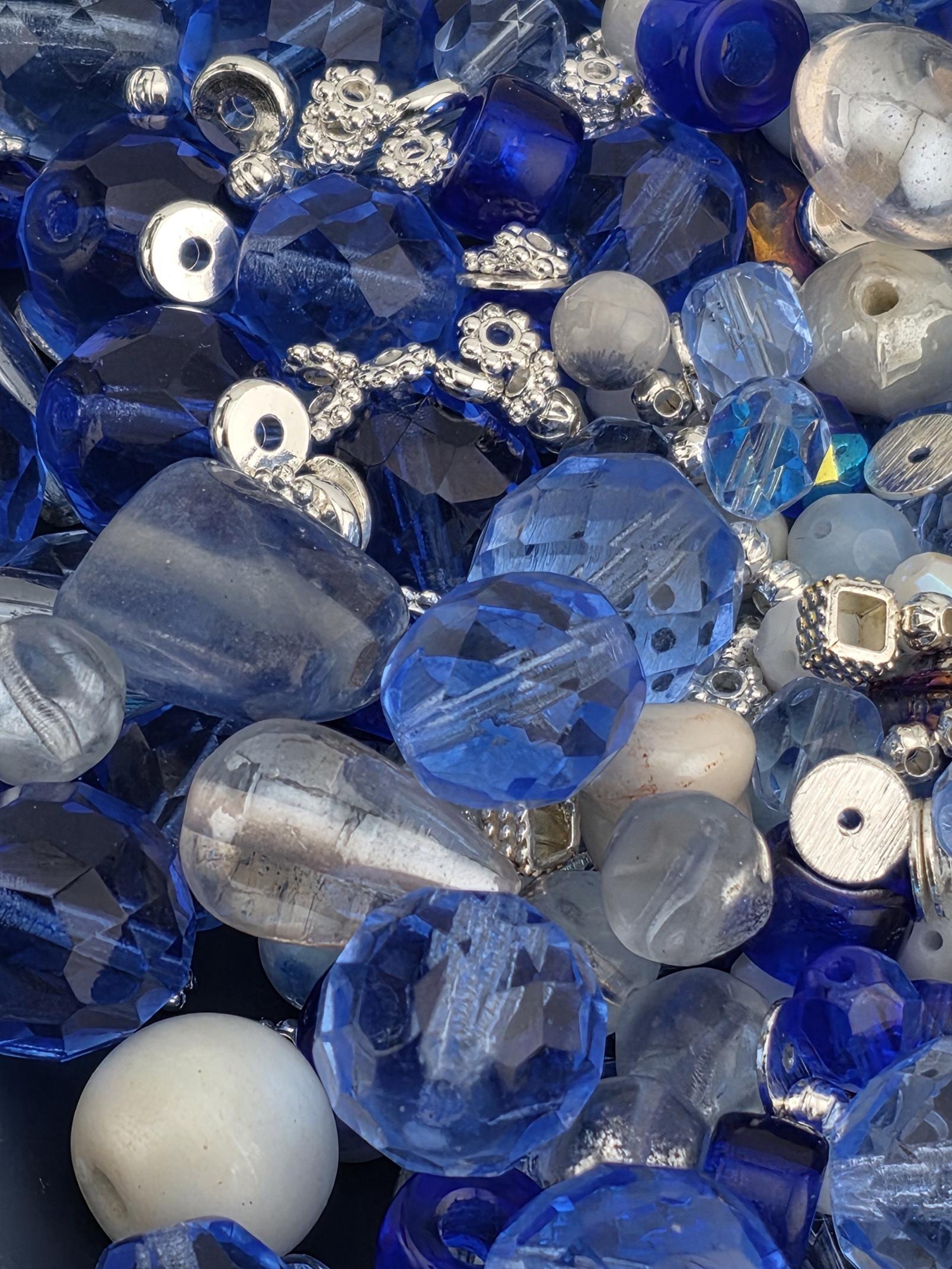 The image is a close-up of various blue and silver beads, including clear beads, glass beads, and metal beads, arranged in a visually appealing manner.