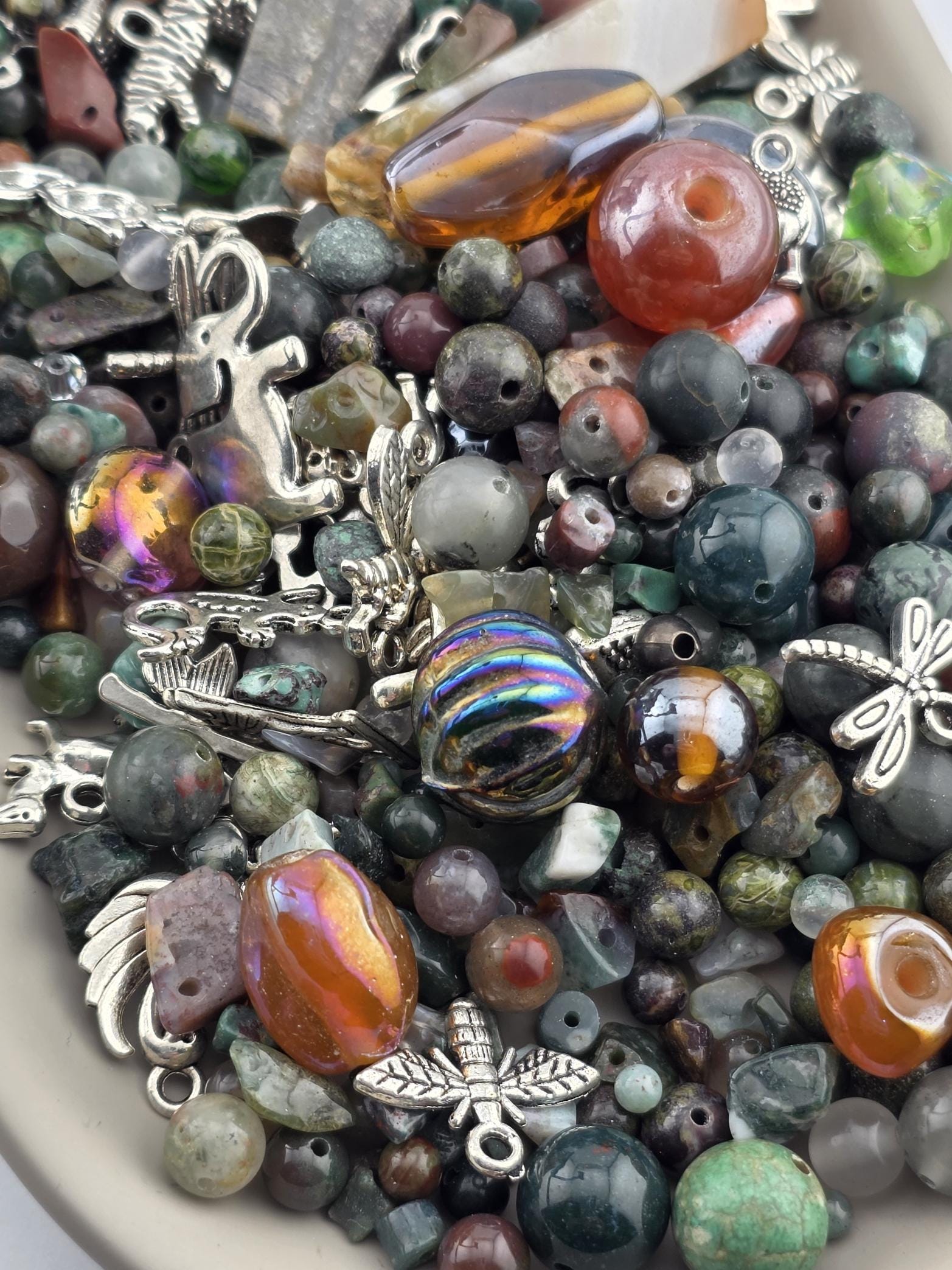 The image is a close-up of a variety of beads, charms, and other decorative items, including glass beads, metal charms, and other colorful objects, all piled together.