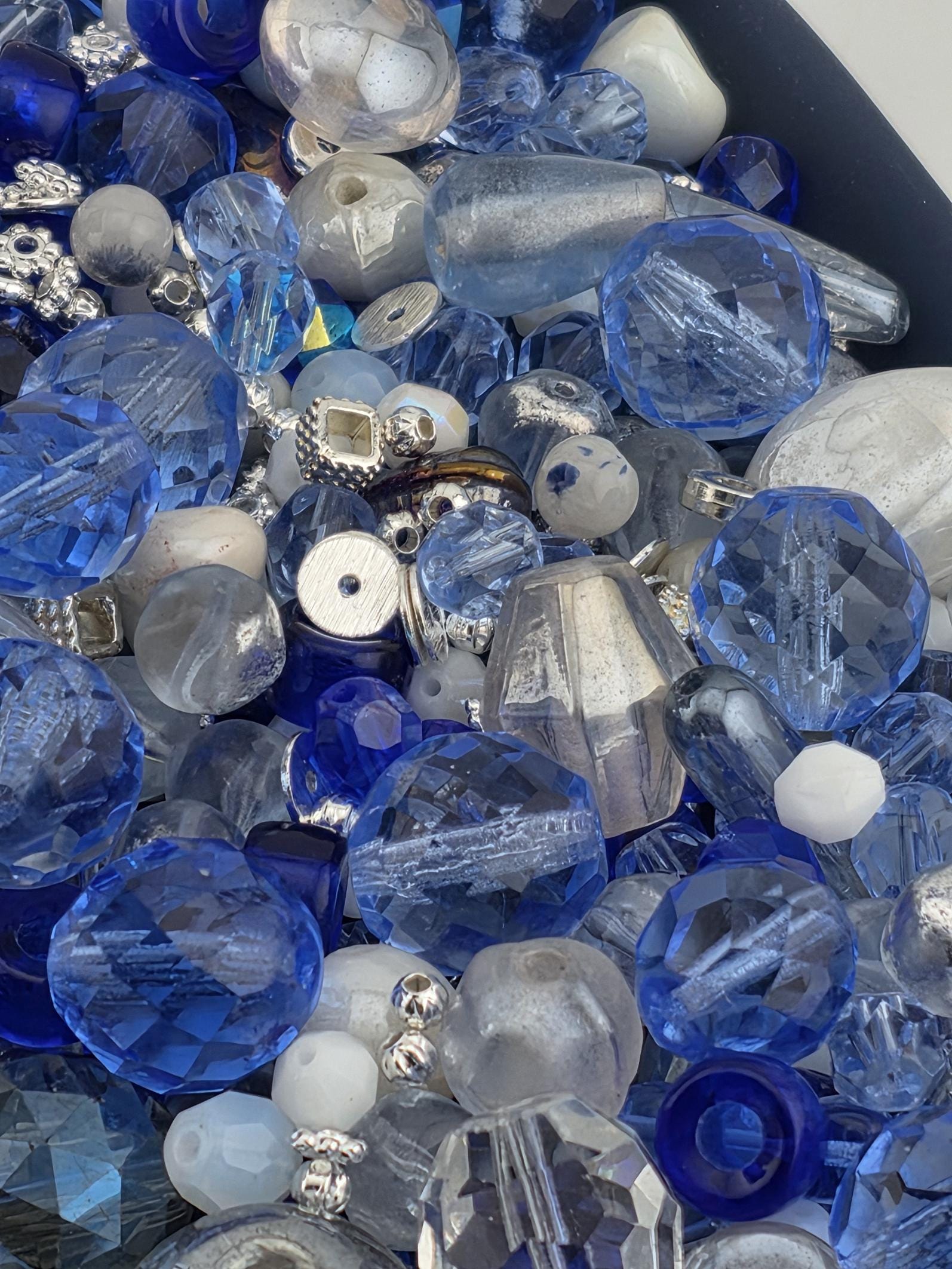 a variety of blue and silver glass beads, including clear, blue, and silver beads, as well as some white beads. The beads are scattered throughout the frame, creating a visually interesting and diverse collection.