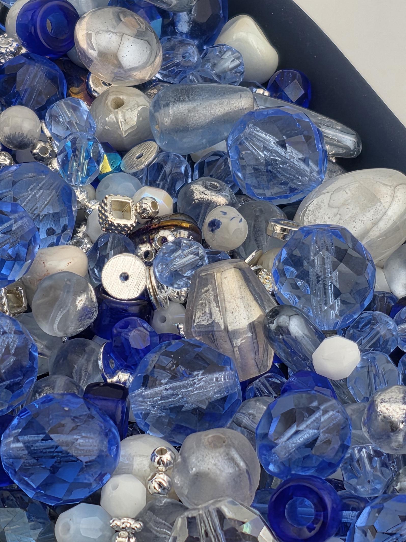 The image is a close-up of various blue and silver glass beads, including clear, blue, and silver beads, as well as some white and silver beads.