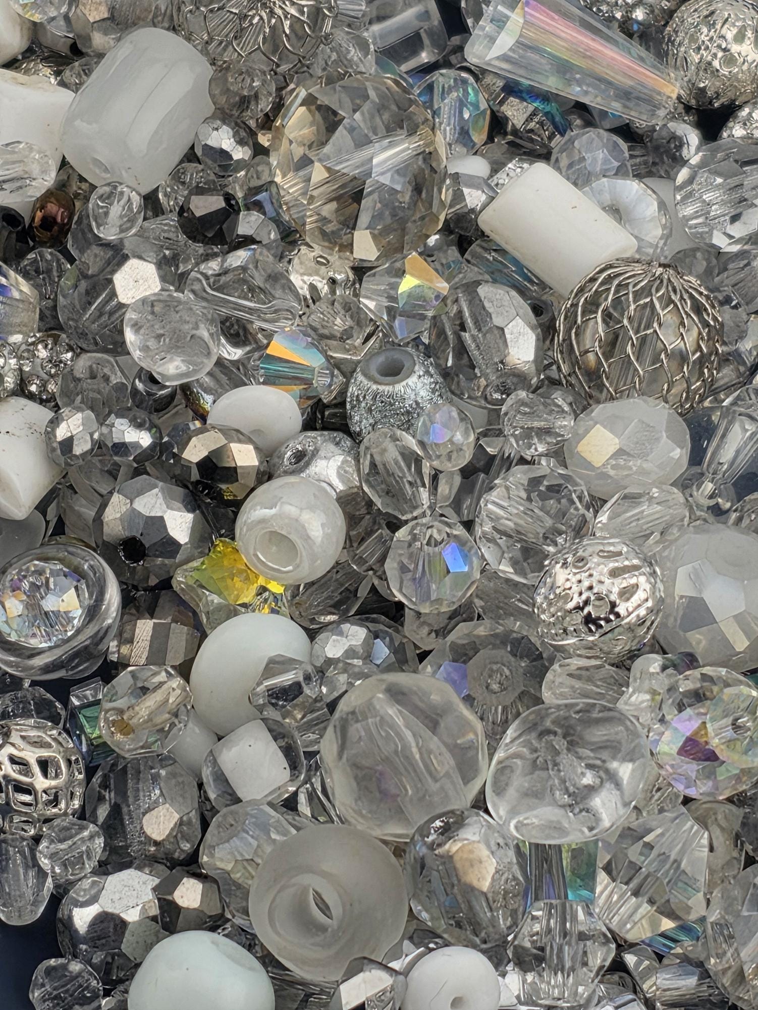 The image is a collection of various glass beads and crystals, including clear, silver, and multicolored pieces, scattered together.