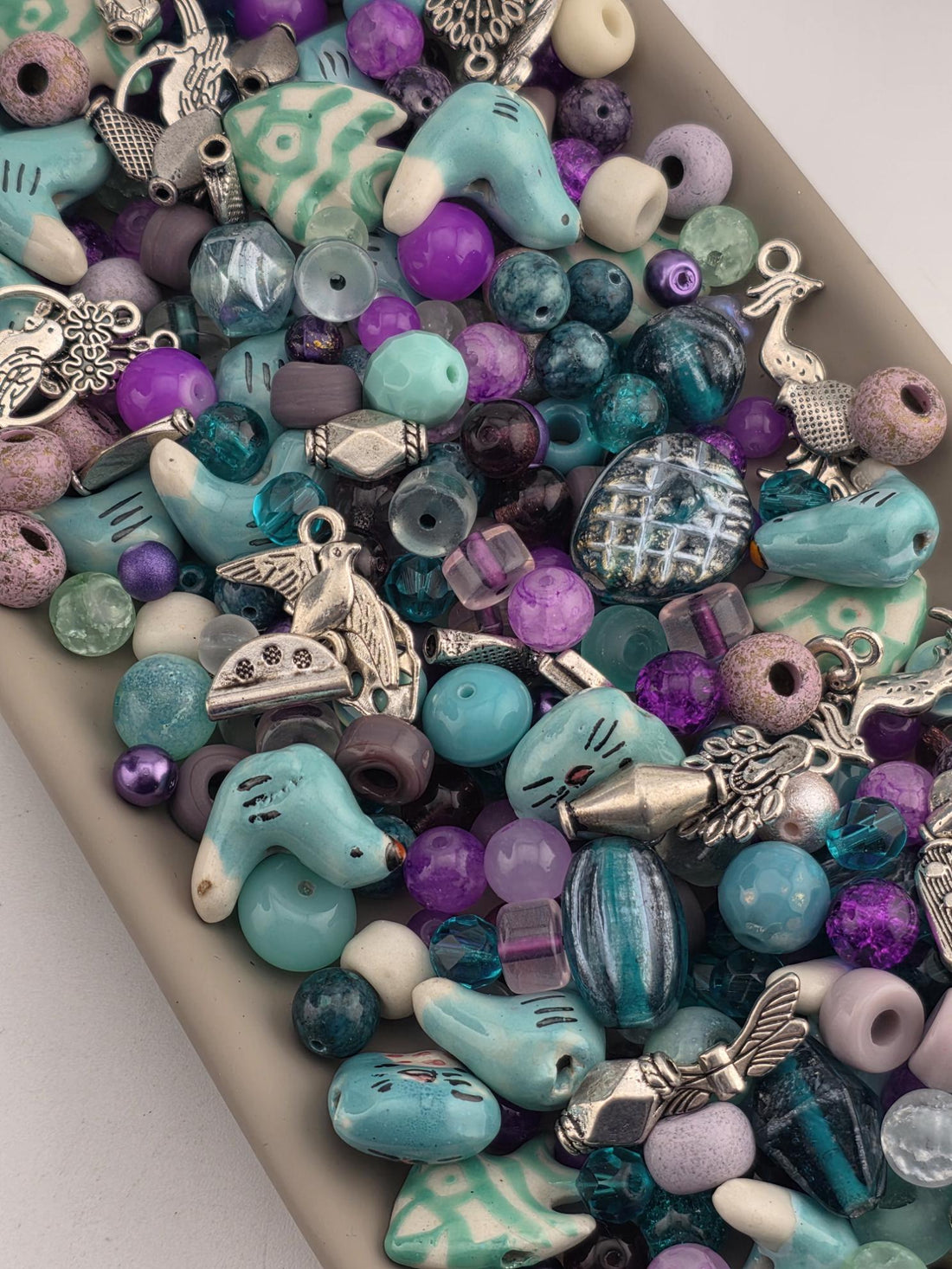 A collection of various colorful beads, charms, and trinkets in shades of blue, purple, and green, arranged in a visually appealing manner.
