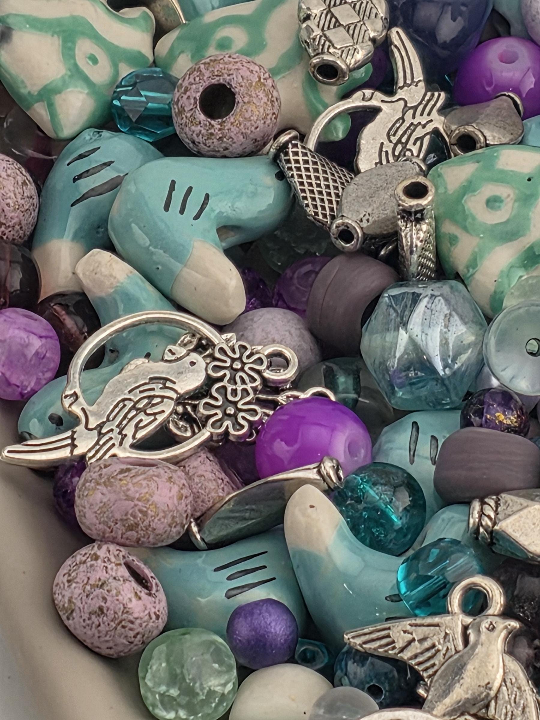 A close-up image of a collection of colorful beads, charms, and other decorative items, including a silver bird charm.