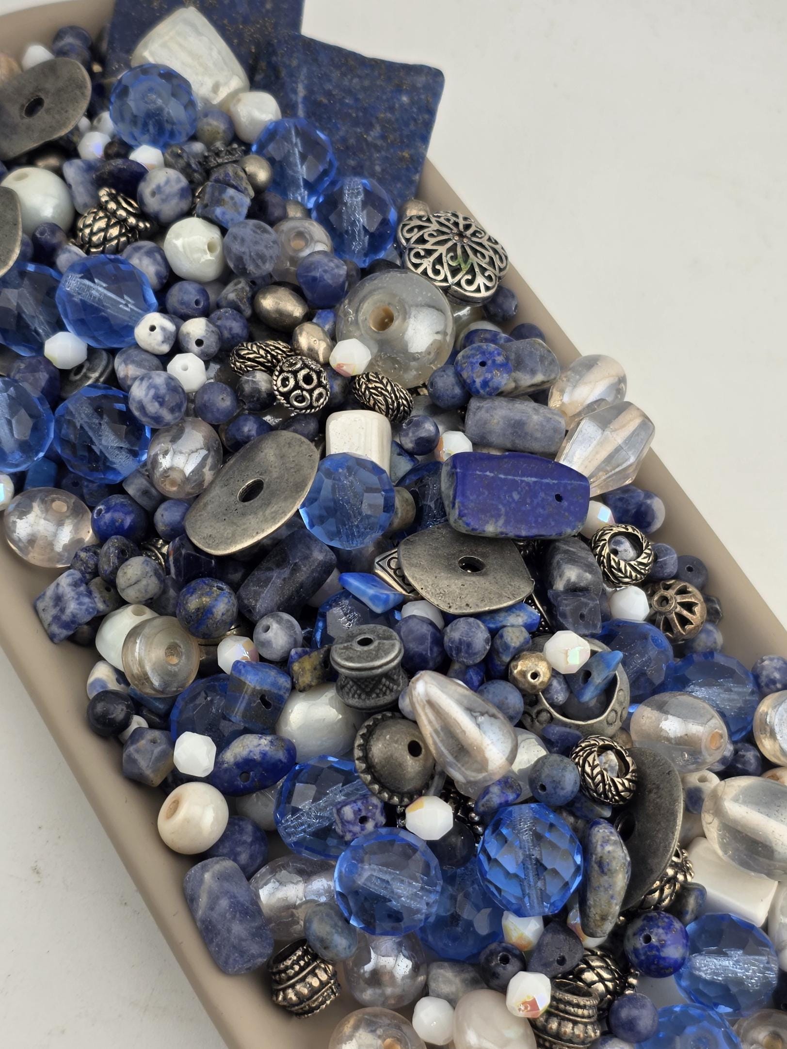 A collection of various blue and silver beads, charms, and other decorative items arranged in a tray or container.