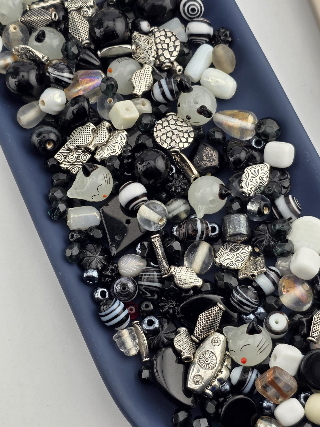 A blue tray filled with various beads, charms, and other decorative items in shades of black, white, and silver.