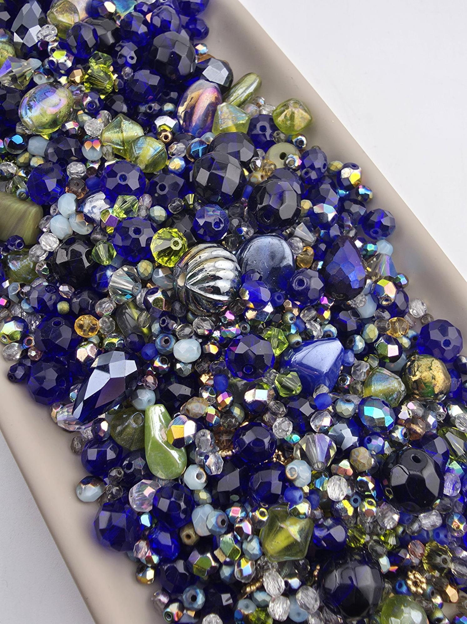 The image is a close-up of a collection of colorful glass beads, including blue, green, yellow, and silver beads, arranged in a visually appealing manner.