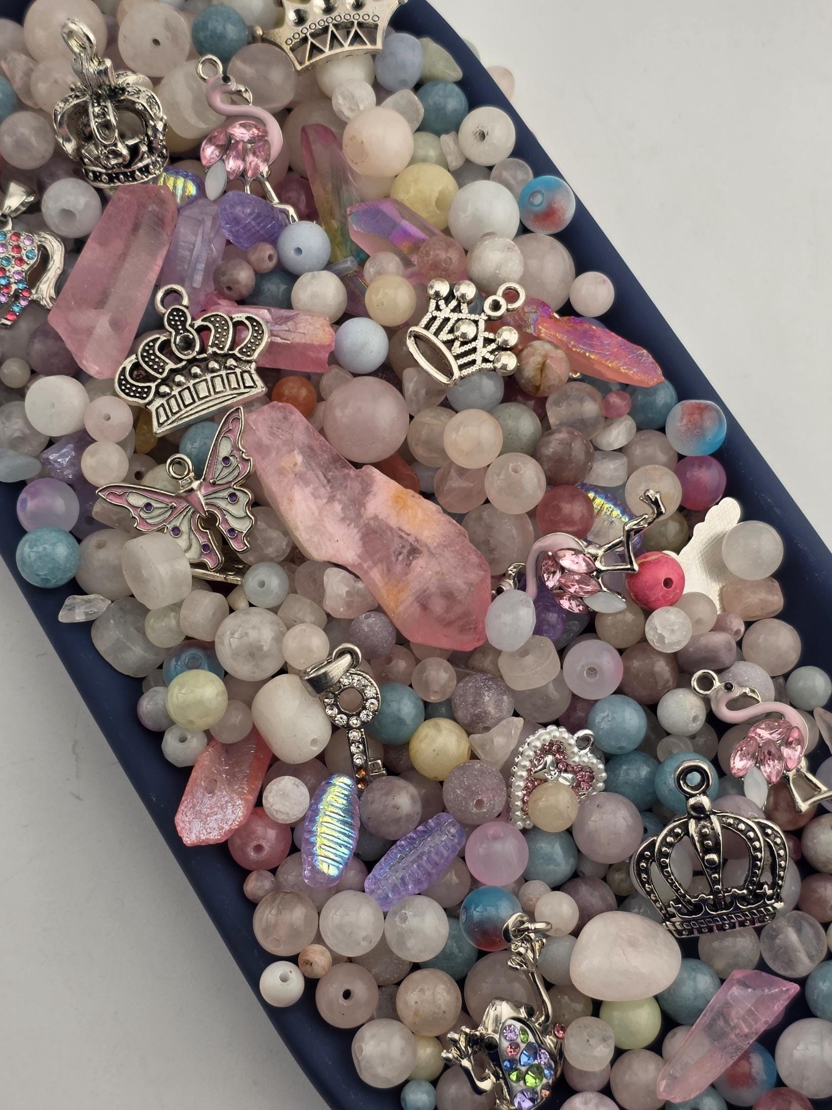 A collection of various beads, charms, and gemstones in a variety of colors and shapes, including crystals, pearls, and gemstones, arranged in a visually appealing manner.