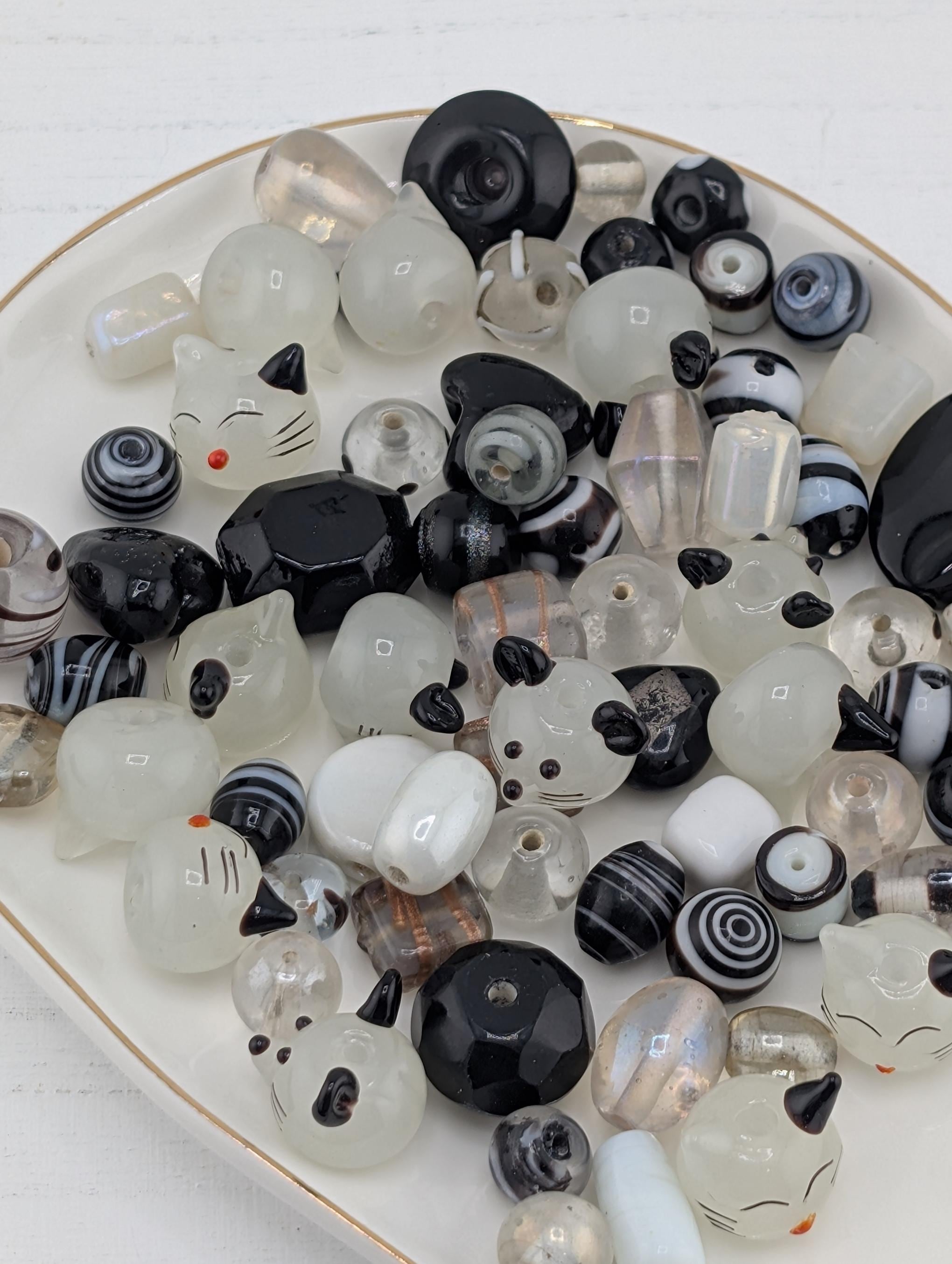 a collection of various beads and glass objects, including black and white beads, clear beads, and some with cat-like designs. The objects are scattered across a white surface, creating a visually interesting and diverse display.