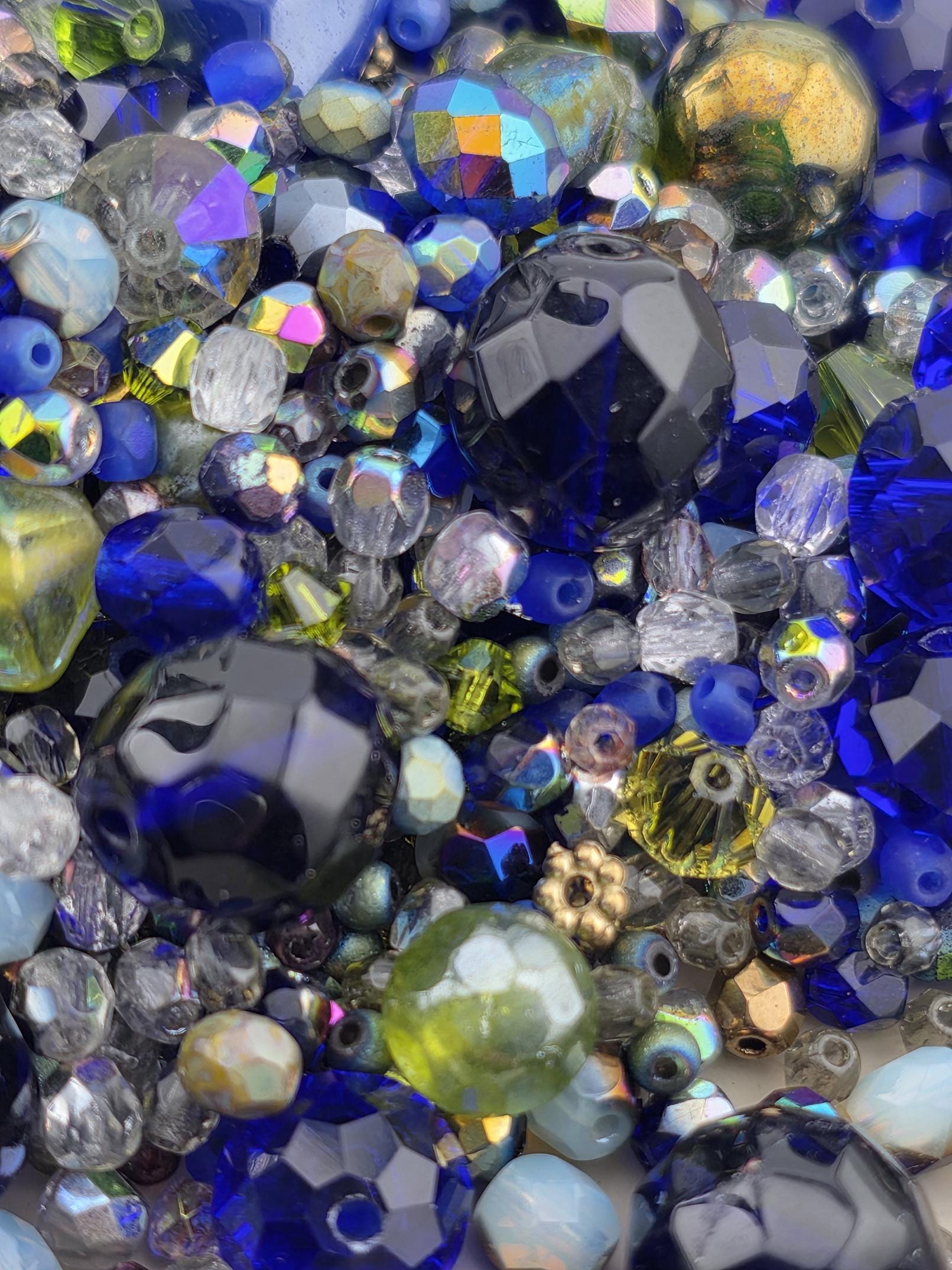The image is a close-up of a collection of various colored glass beads, including blue, green, yellow, and clear beads, creating a visually striking and vibrant display.