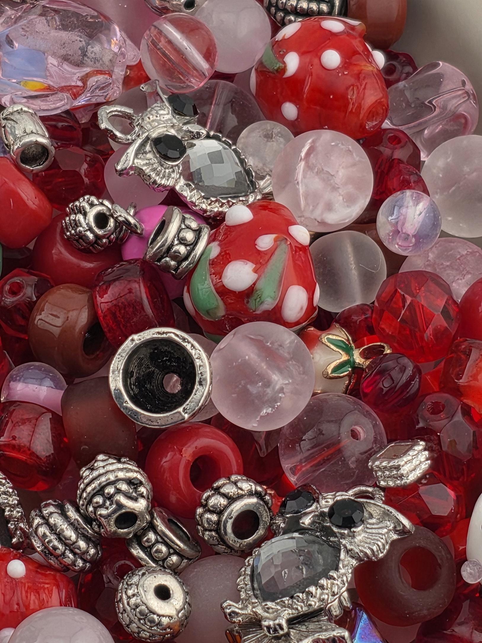 A colorful assortment of beads, charms, and glass objects in various shapes and sizes, including red, pink, and silver elements.