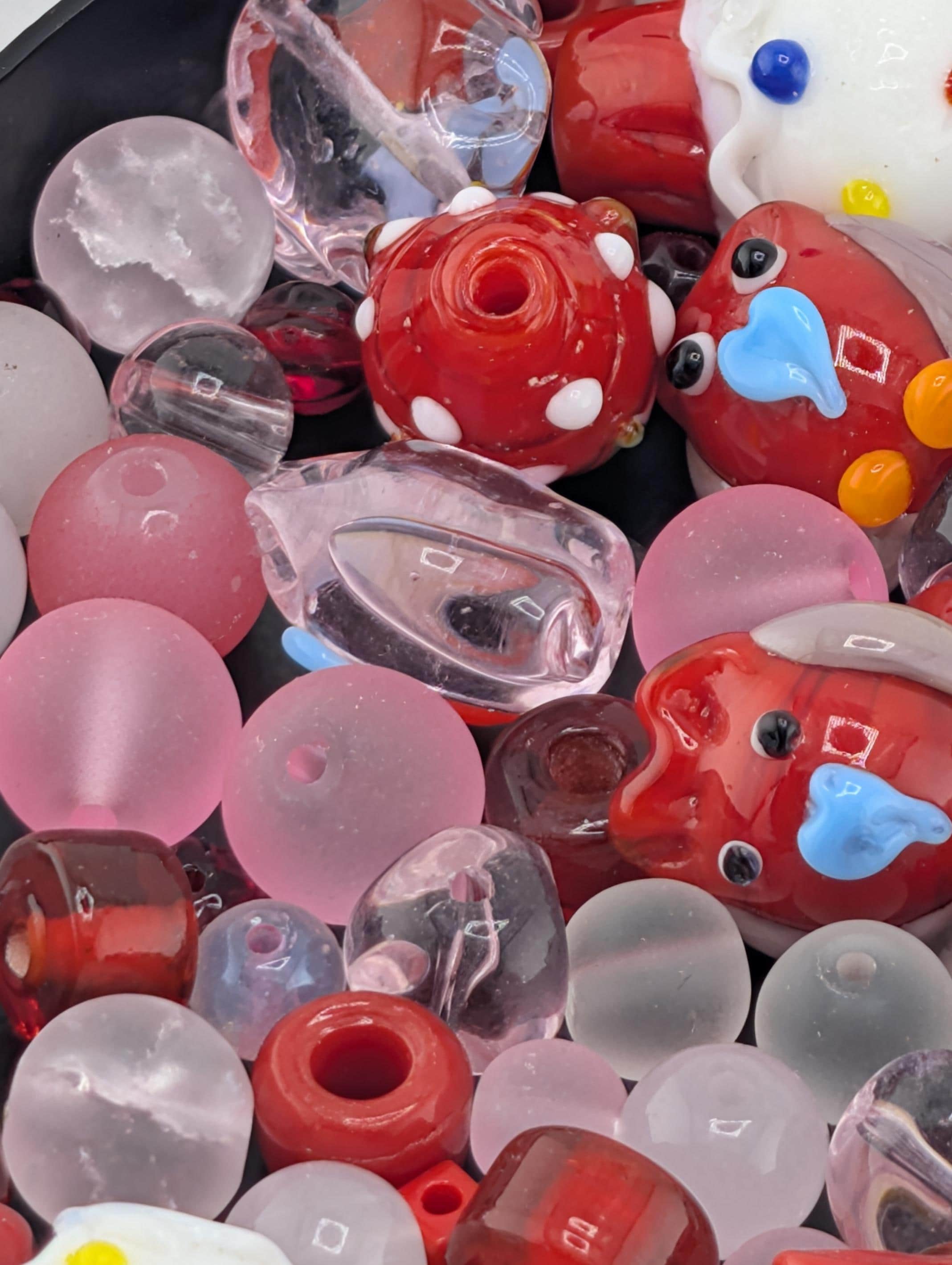 a variety of colorful glass beads, including clear, red, and pink beads, as well as some with blue and yellow accents. The beads are scattered across a surface, creating a visually appealing and diverse collection.