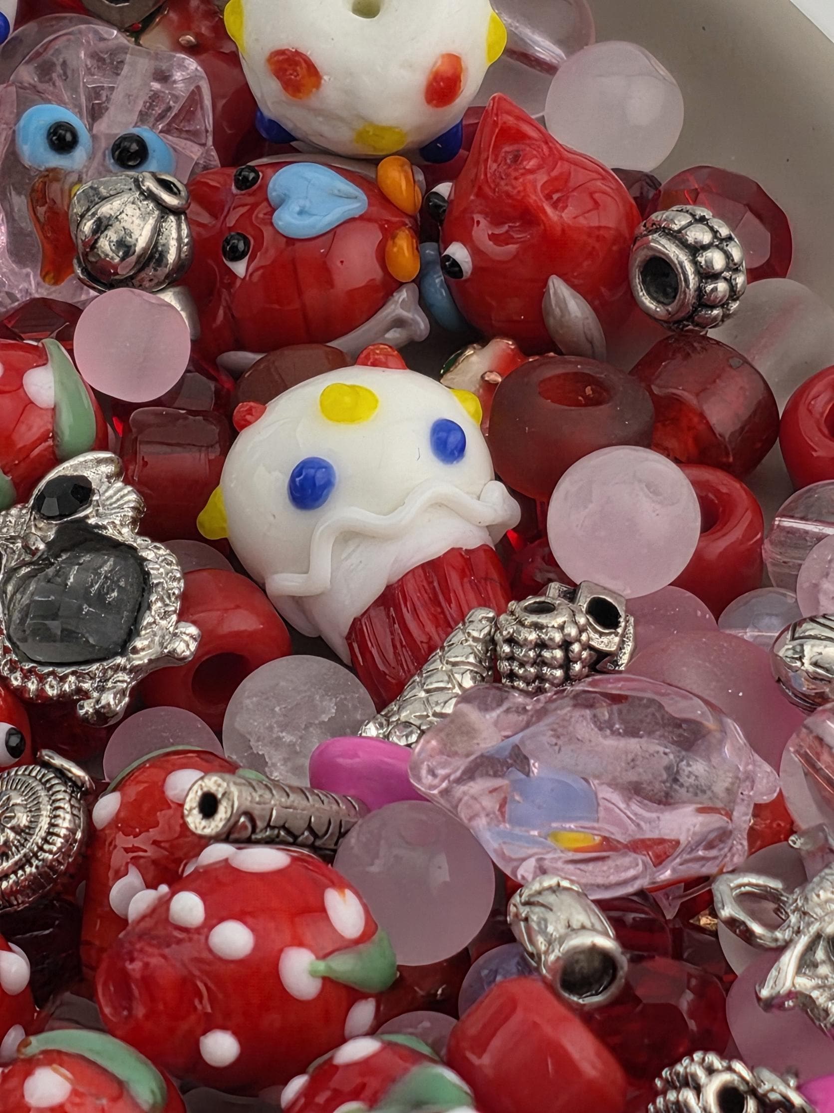 A colorful assortment of beads, charms, and other decorative items, including red and white polka dots, glass beads, and metal ornaments, are scattered together in the image.