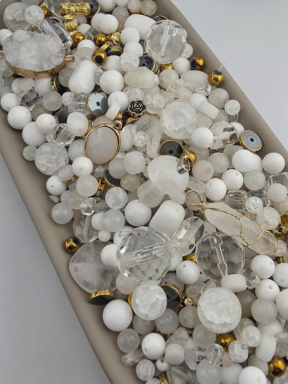 The image is a collection of various white and clear beads, charms, and other decorative items arranged on a surface.