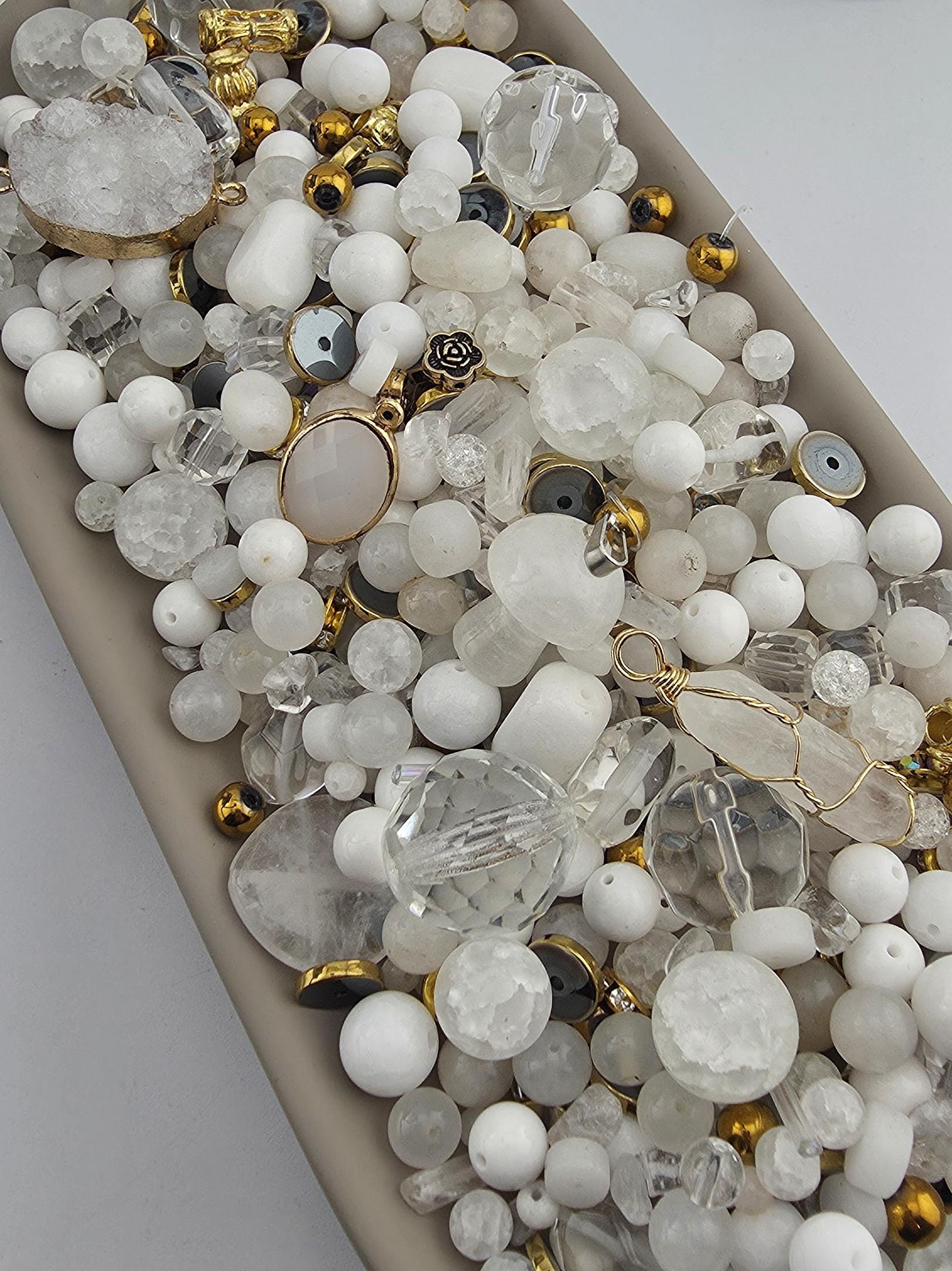The image is a collection of various white and clear beads, charms, and other decorative items arranged on a surface.