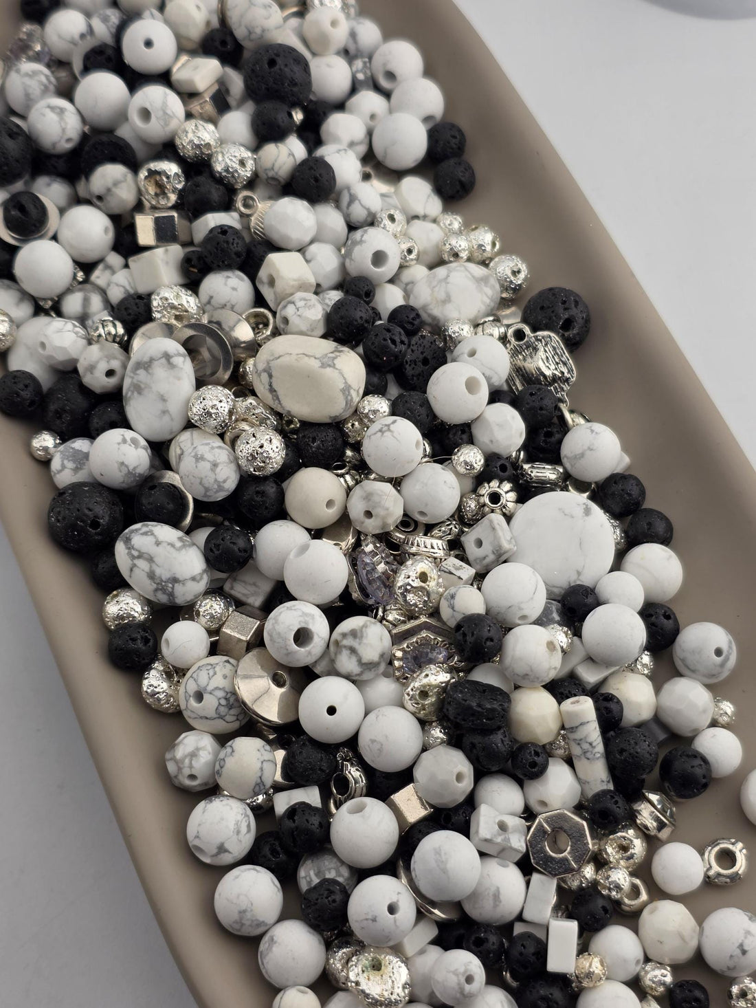 A collection of various beads, charms, and stones in shades of white, black, and silver, arranged on a surface.