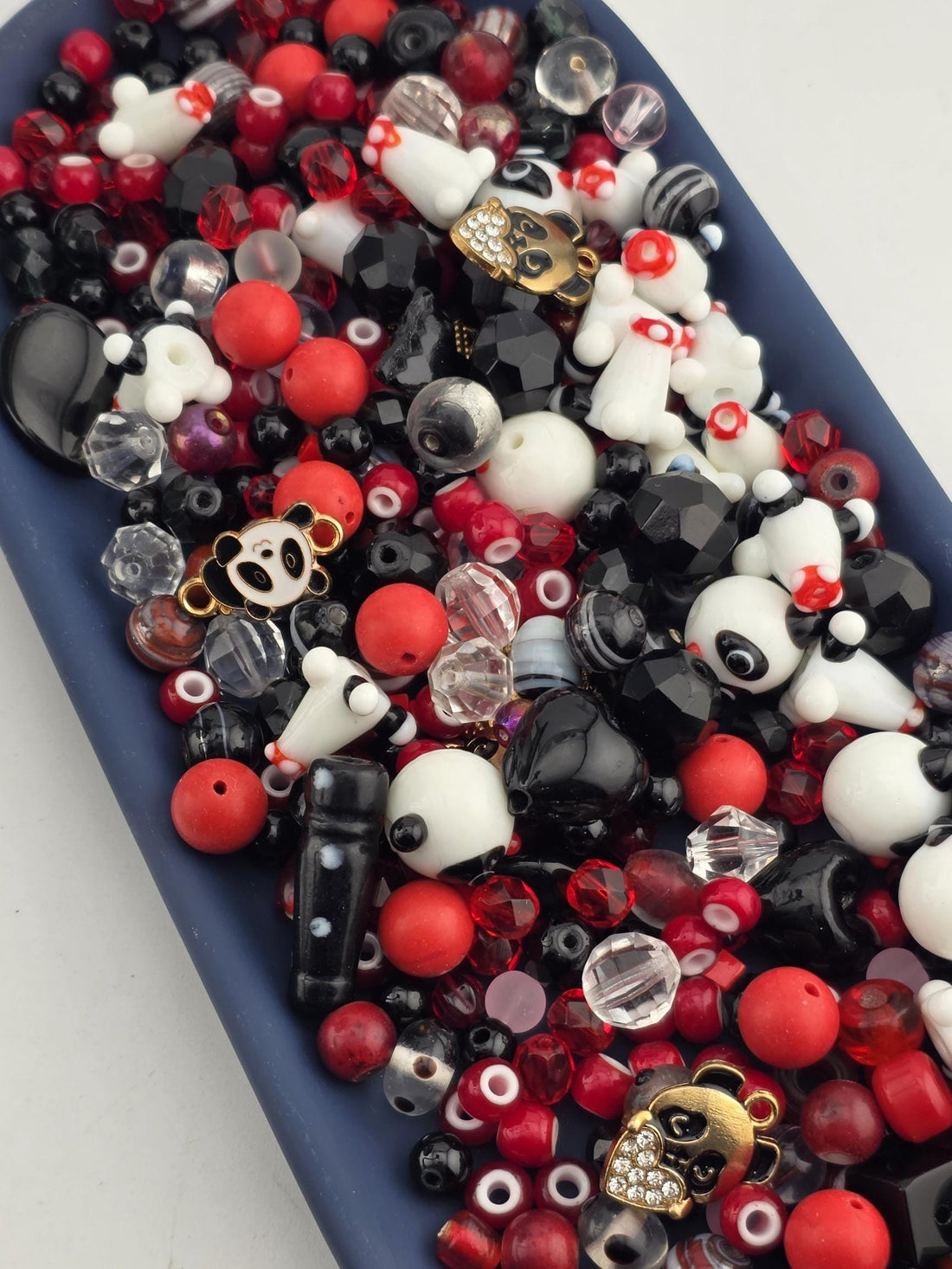A blue tray filled with various beads, charms, and other decorative items in shades of red, black, and white.