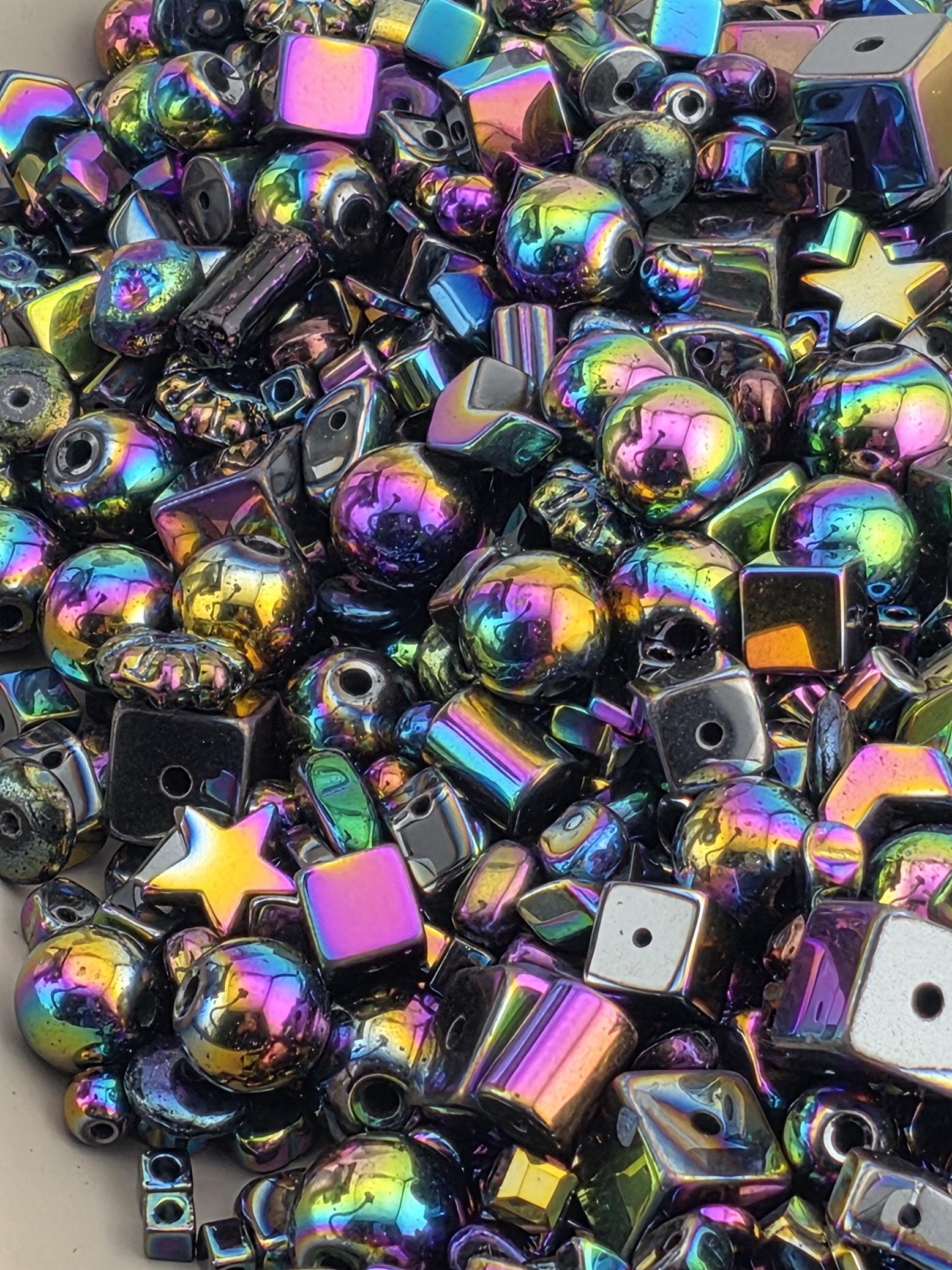 The image is a close-up of a collection of colorful beads and shapes, including various metallic and gemstone-like elements.