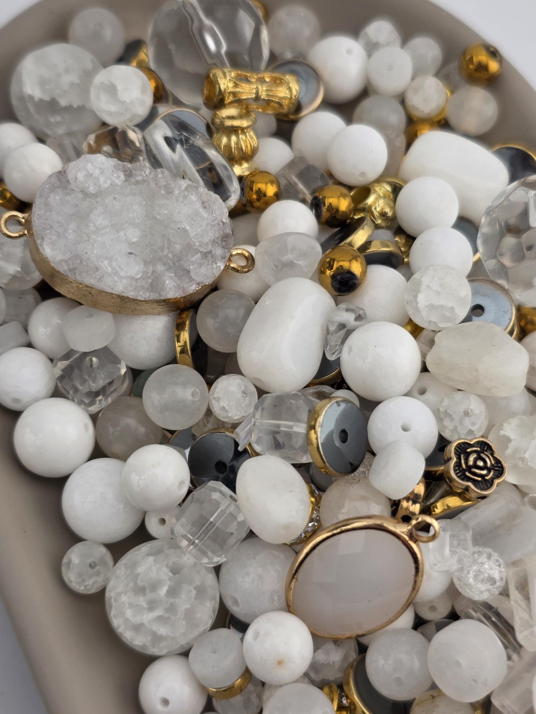 The image is a collection of various beads and charms, including clear beads, gemstones, and metal pieces, arranged in a visually appealing manner.