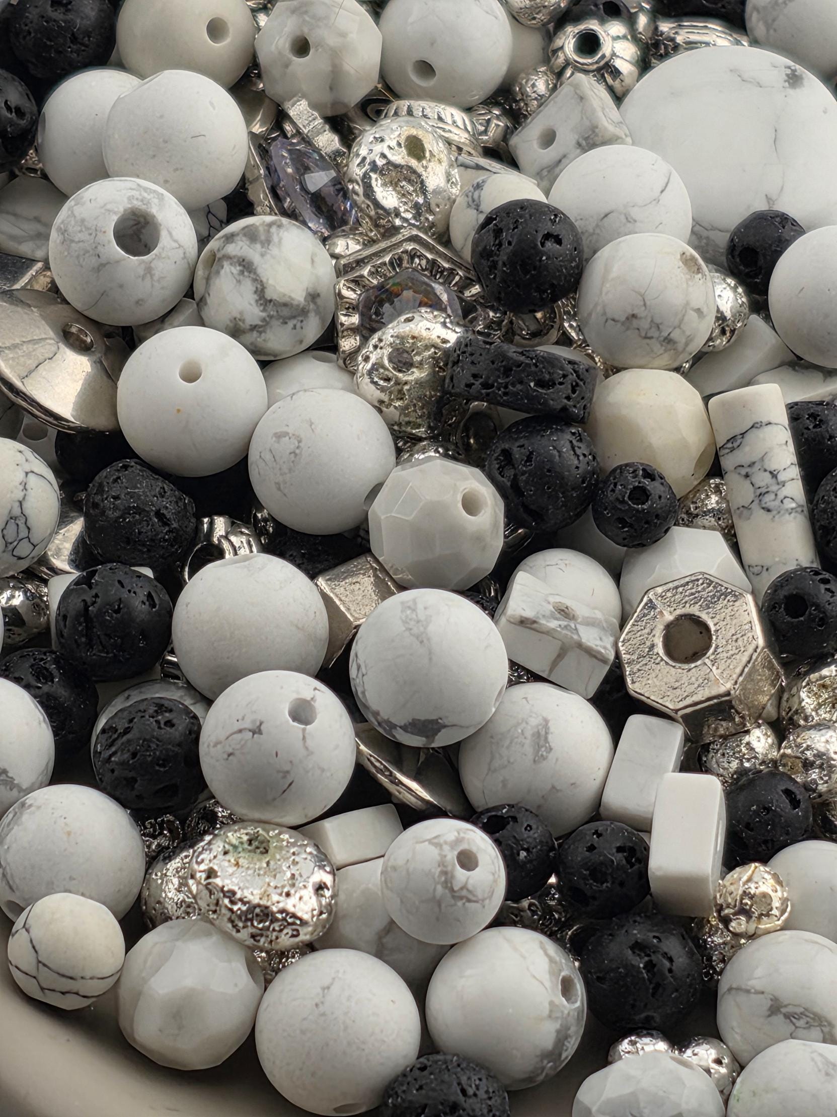 The image is a close-up of various beads and stones, including white, black, and silver beads, as well as some larger stones.