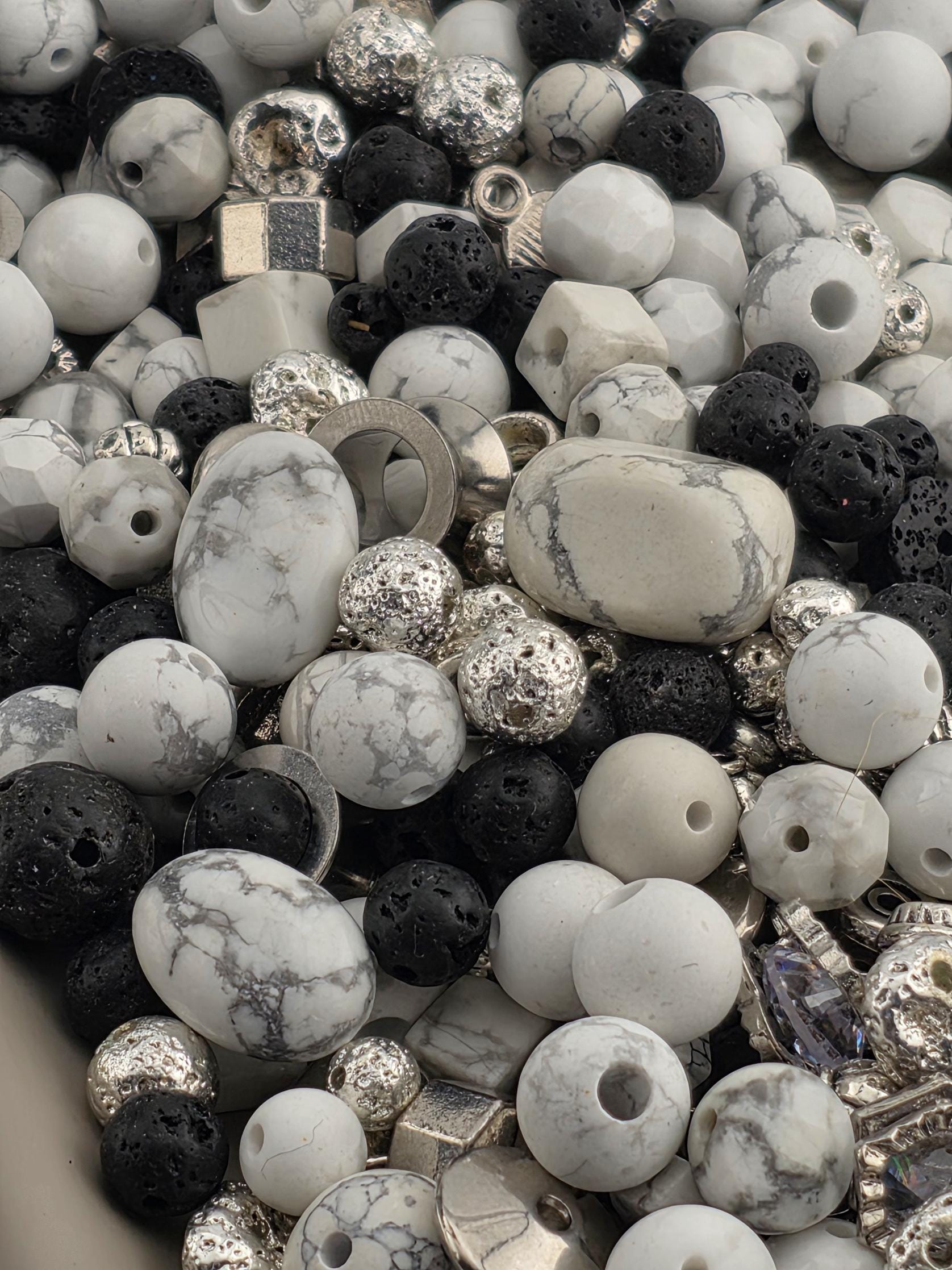 The image is a close-up of various beads and stones, including white, black, and silver beads, as well as some larger stones.