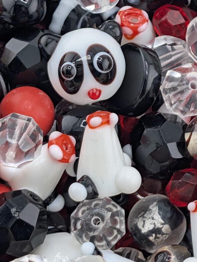 The image is a close-up of a collection of various colorful beads, including clear, black, red, and white beads, as well as a panda-shaped bead.