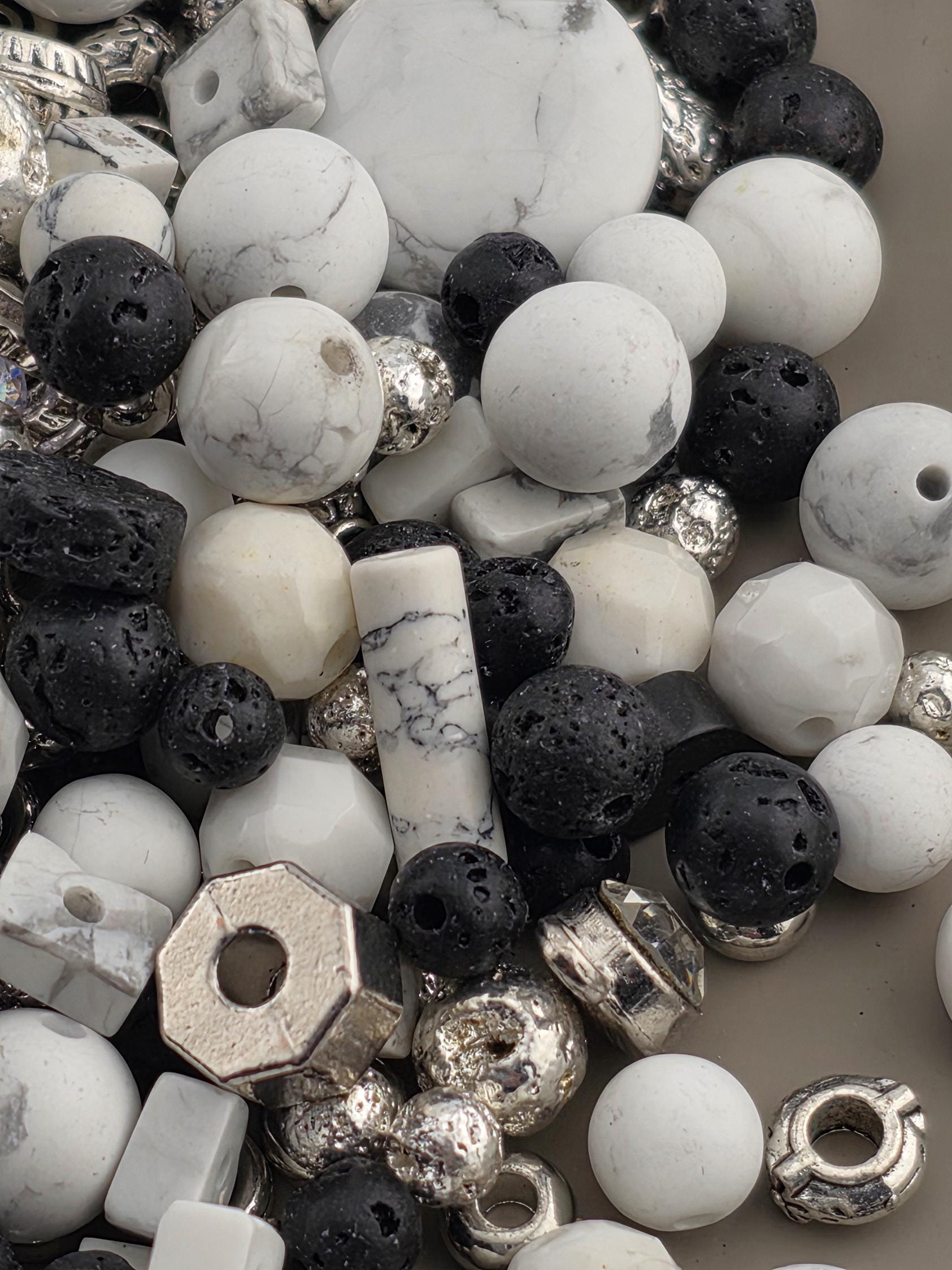 The image is a close-up of various beads and stones, including white, black, and silver beads, as well as some larger stones.