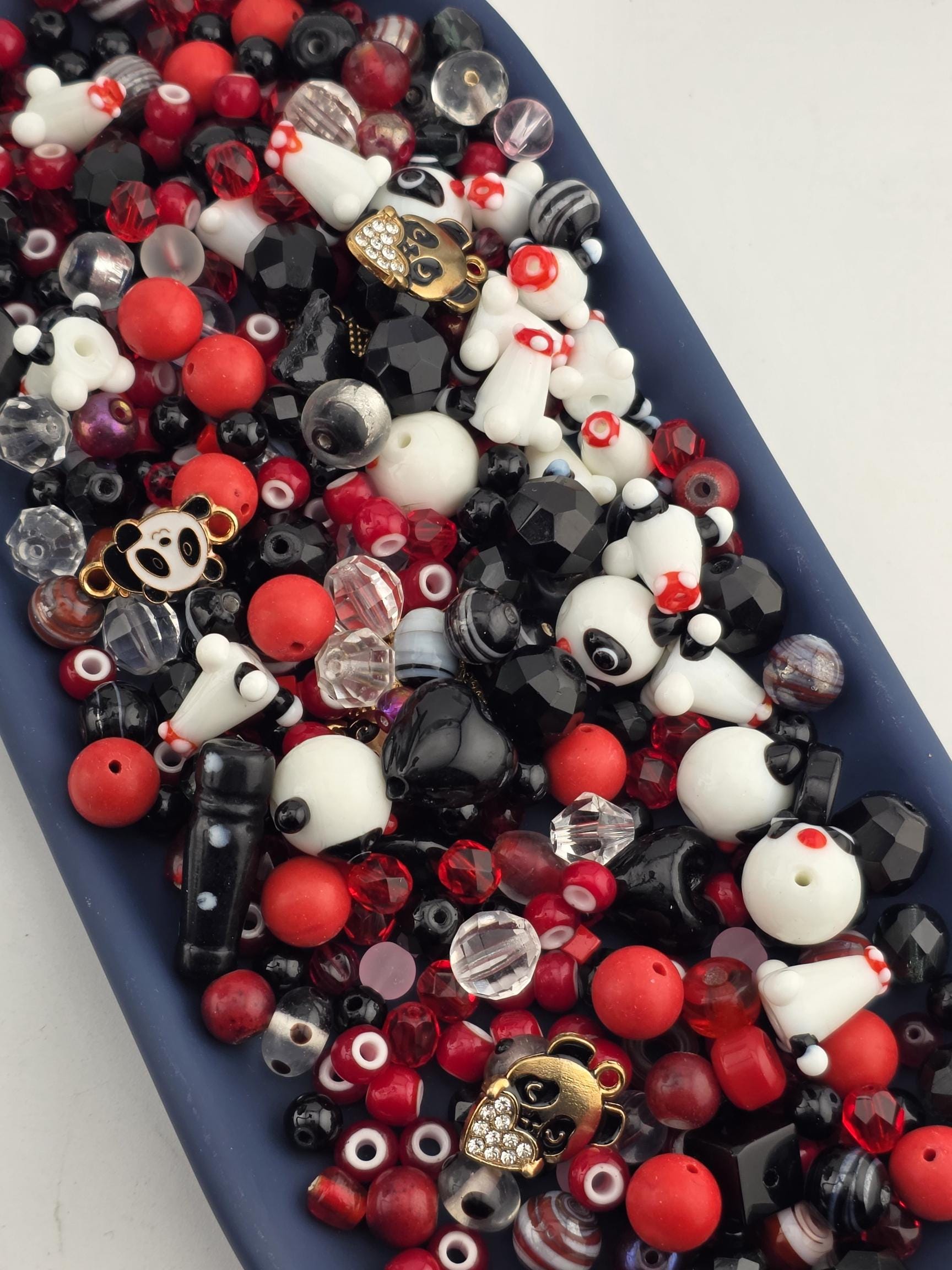 A collection of various beads, charms, and beads in different colors, including red, black, white, and clear beads, as well as some with panda and skull designs.