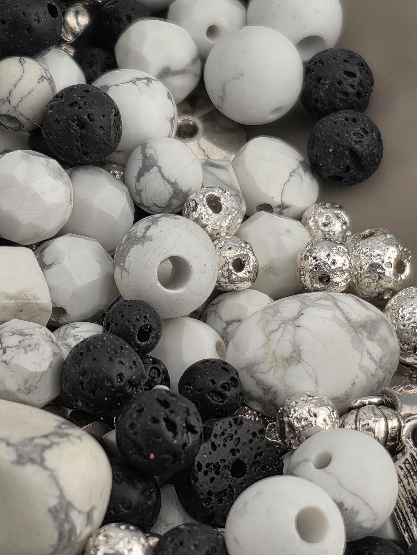 A close-up image of various beads and stones, including white, black, and silver beads, arranged in a visually appealing manner.
