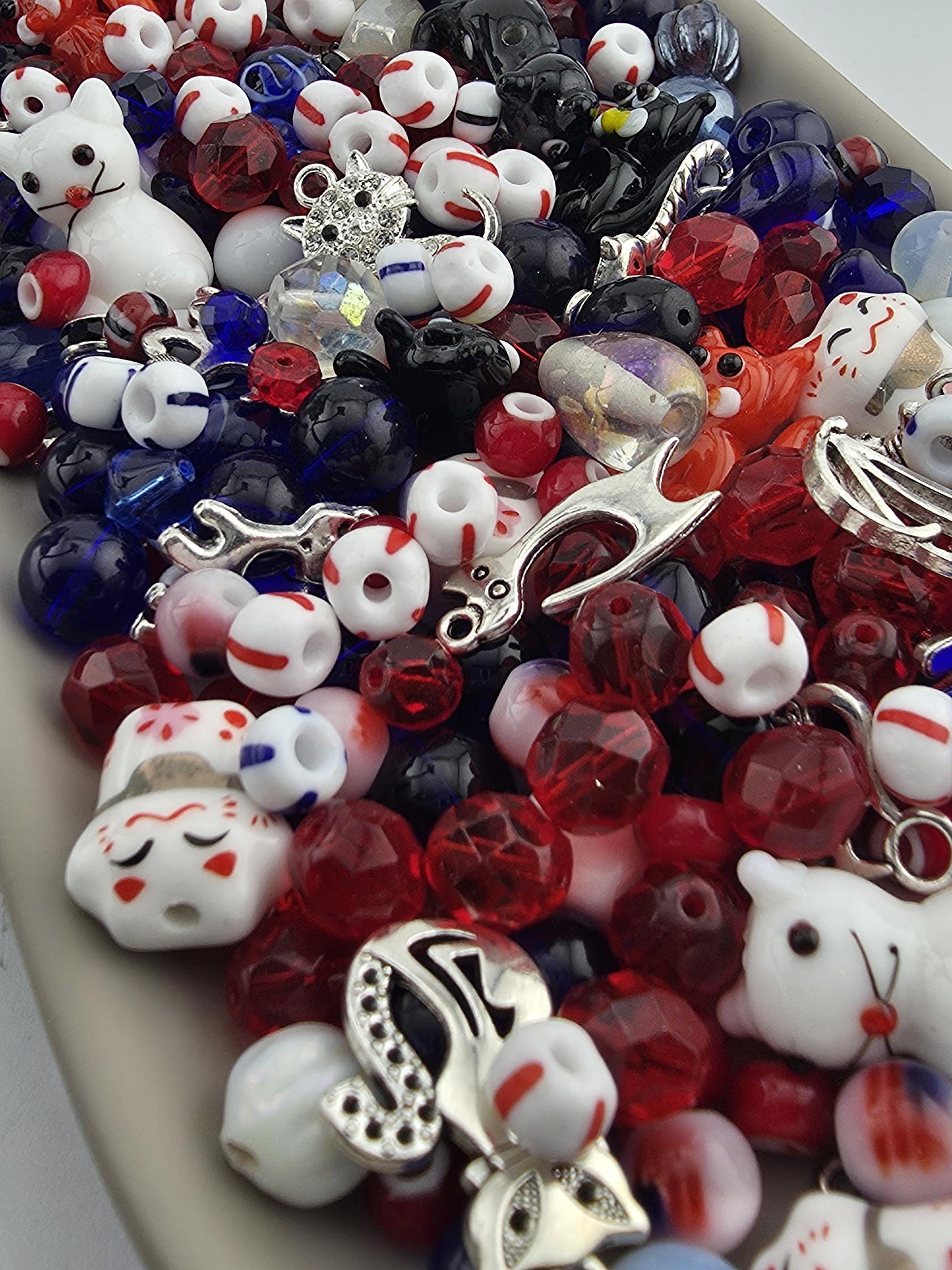 A colorful assortment of beads, charms, and other decorative items, including red, white, and blue beads, as well as silver and black charms, are scattered across the image.