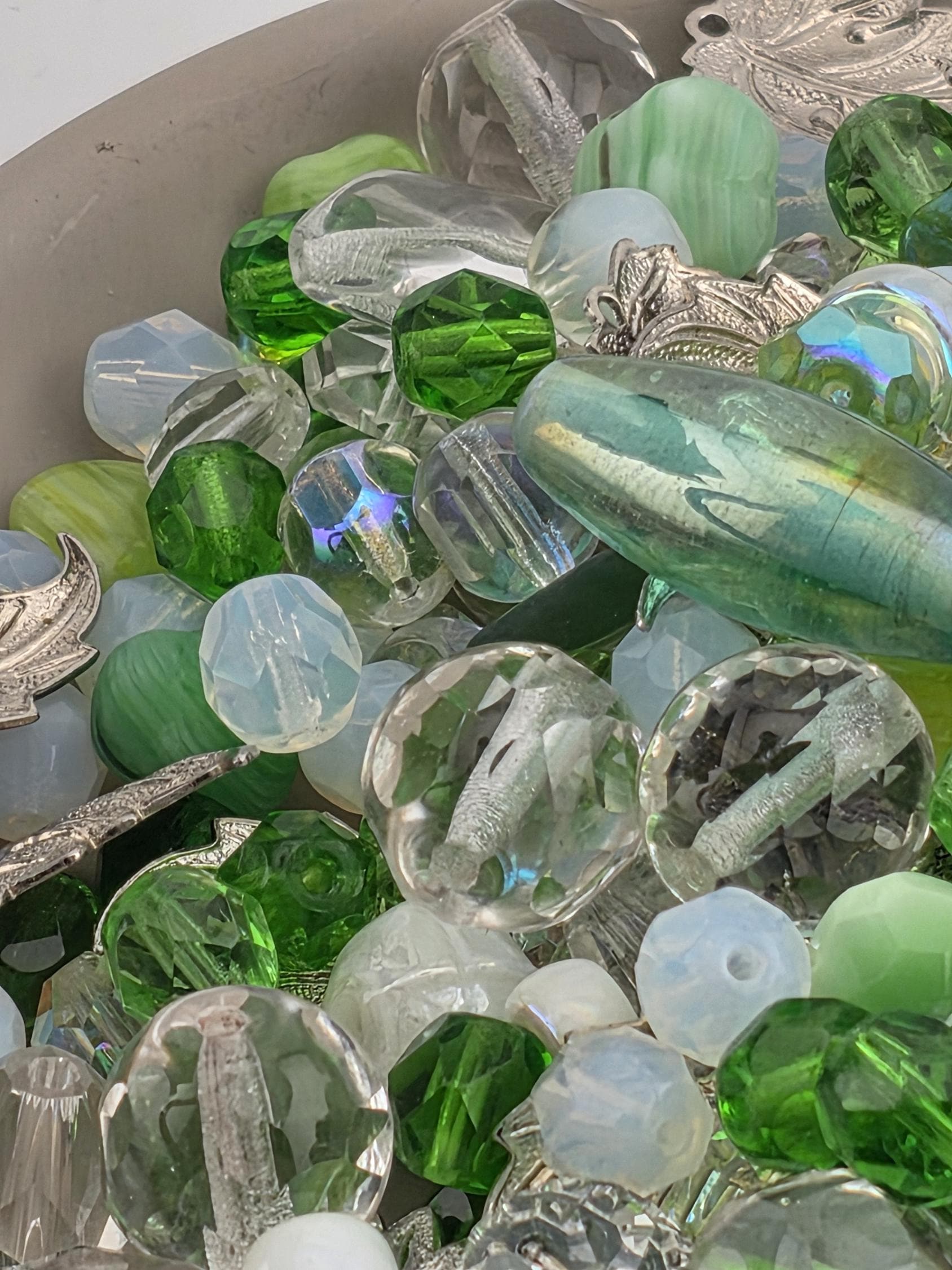 The image is a close-up of various glass beads and stones, including clear, green, and silver-colored pieces.